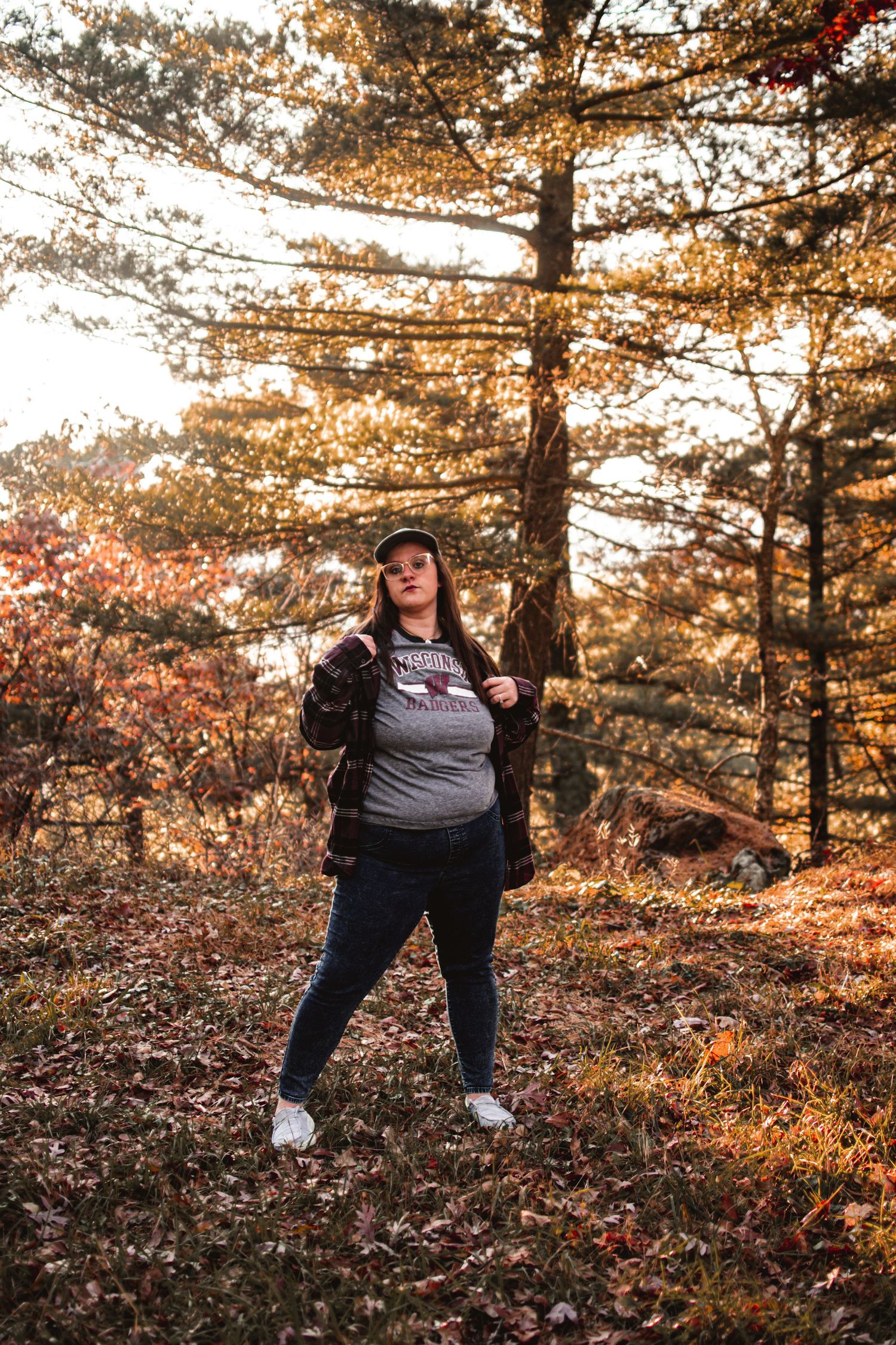 Individual in casual wear poses confidently in autumn forest setting.