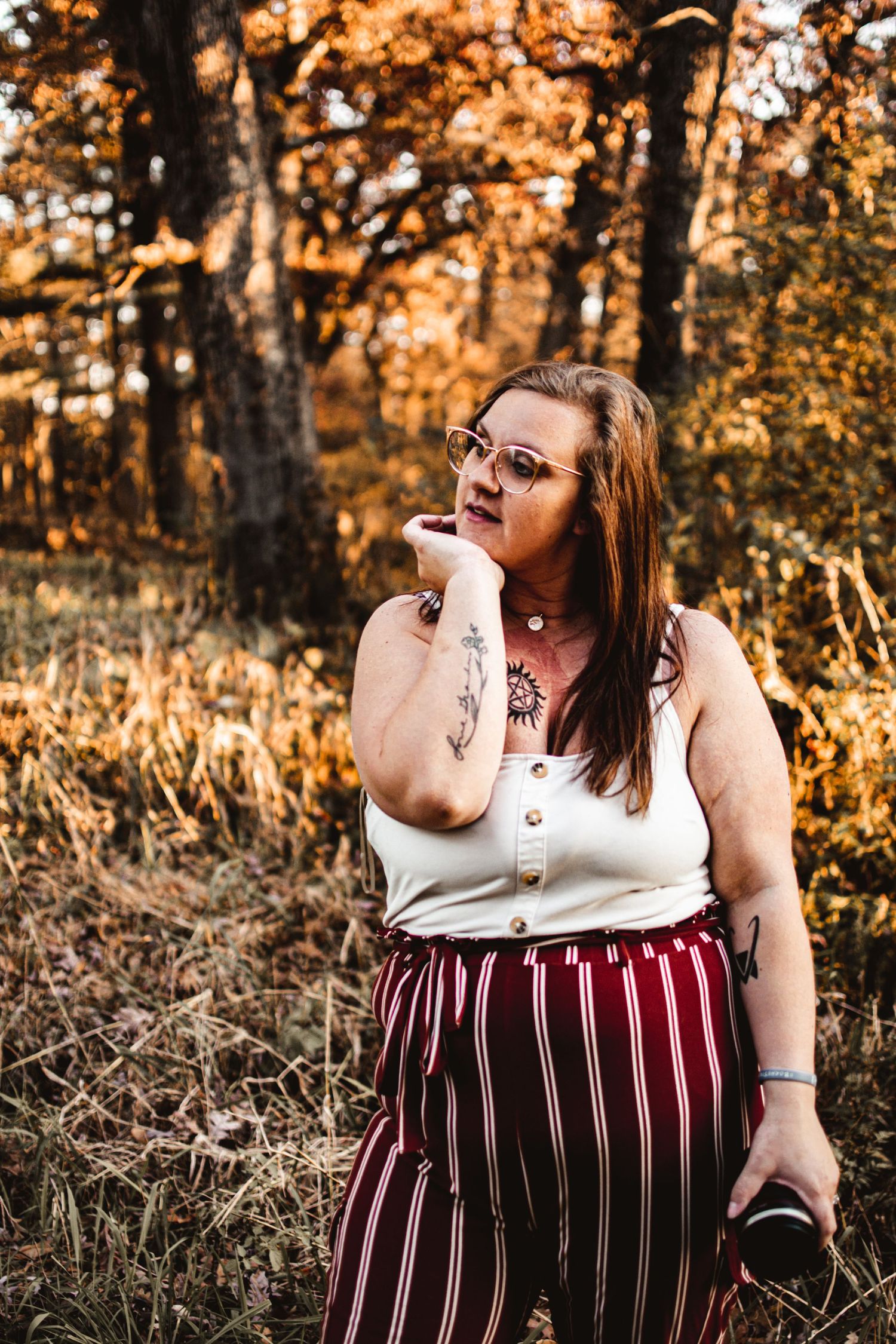 Individual in striped pants and white top poses in autumn forest setting.