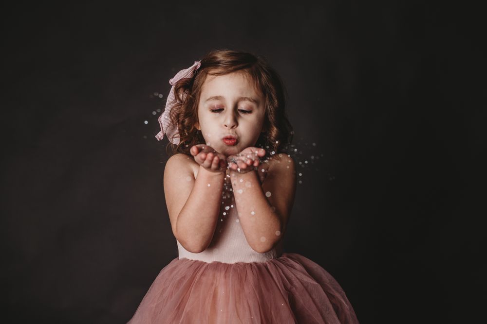 Pink dress and glitter create a dreamy portrait session against a dark background.