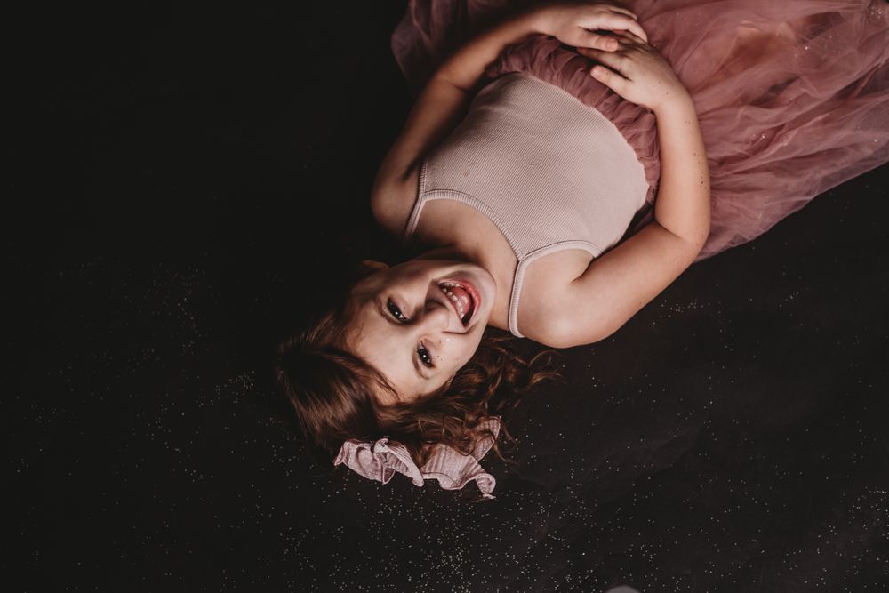 Artistic portrait of child in pink dress reclining on dark studio floor.