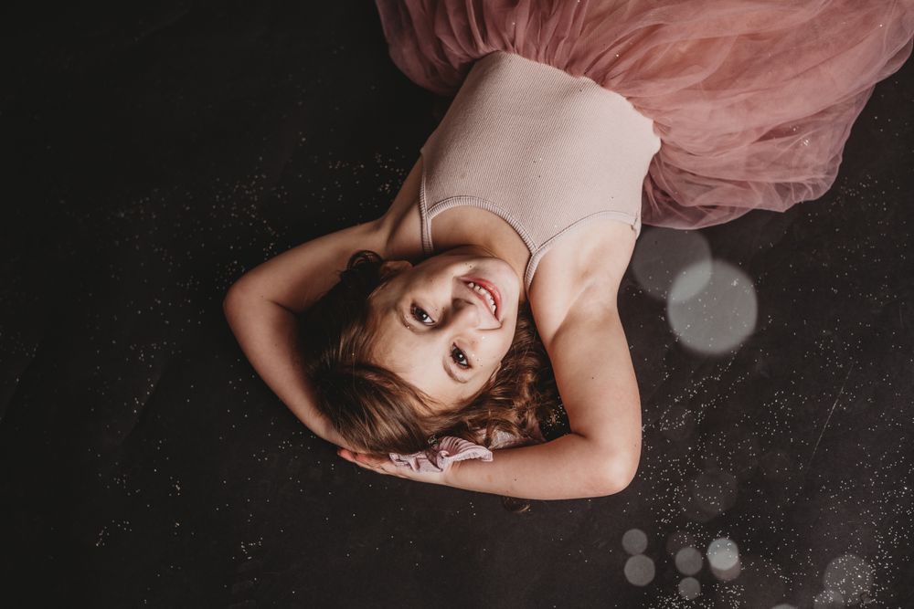 Dreamy studio portrait with child in pink dress against dark background.