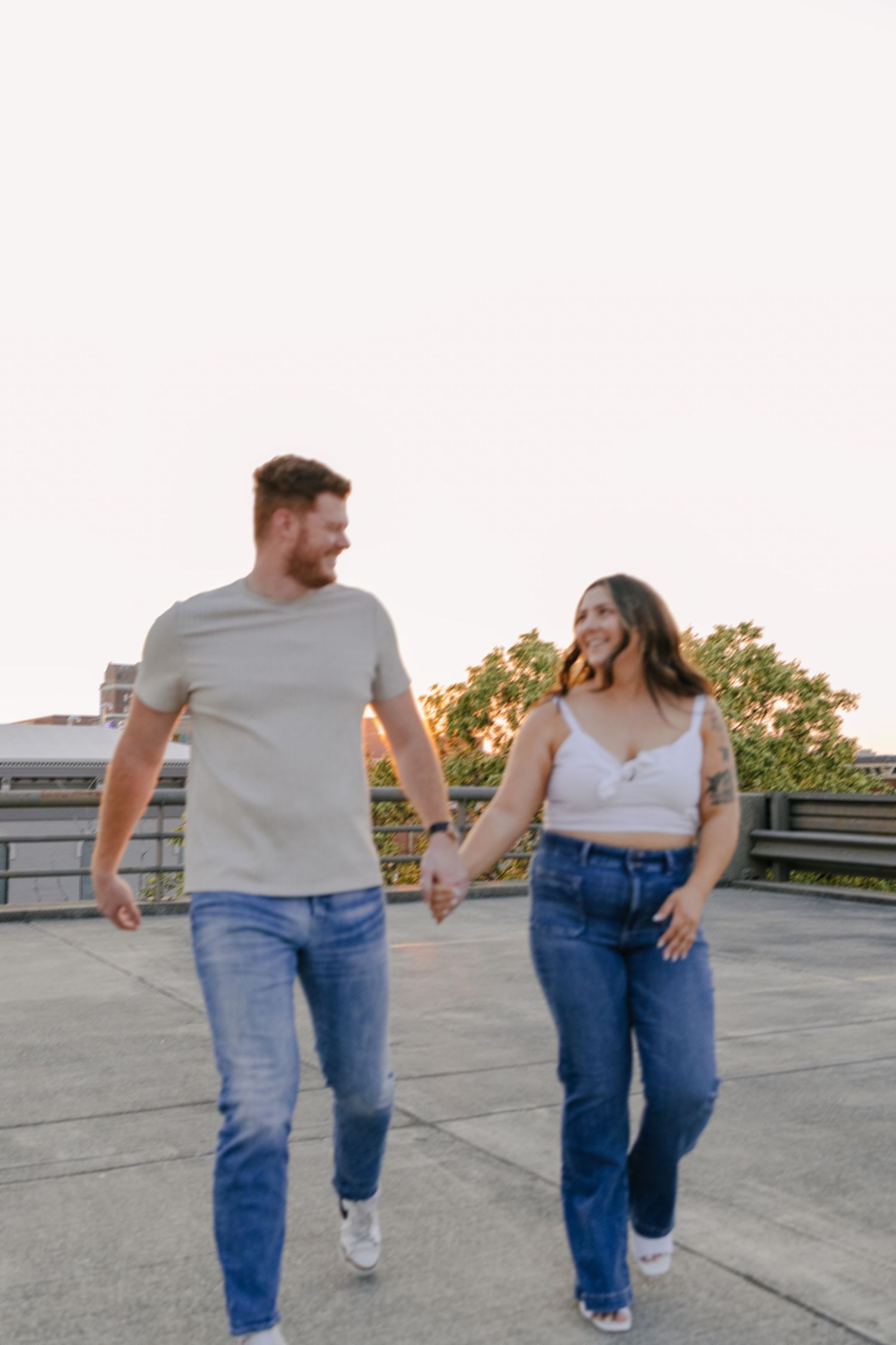 Couple in casual attire walking hand in hand on a rooftop during golden hour.