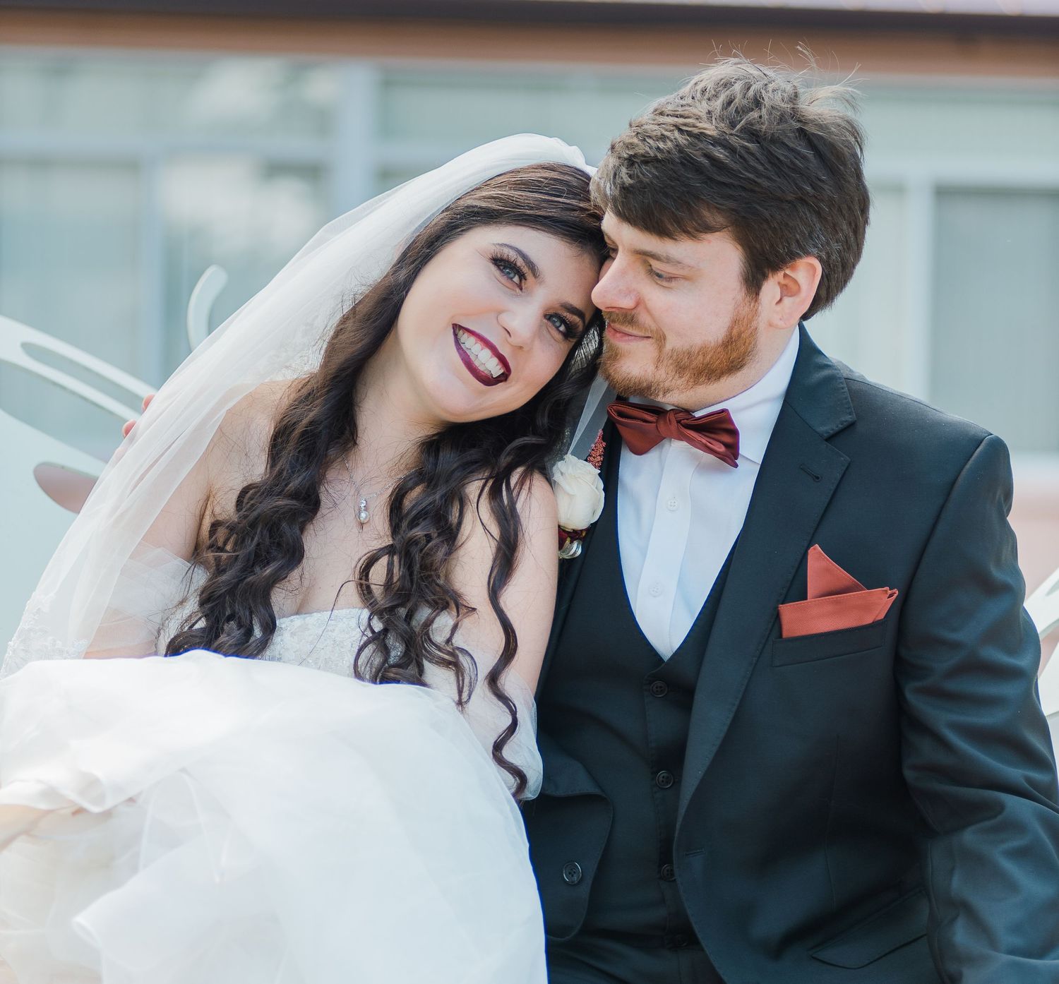 A joyful wedding portrait featuring a bride in white and groom in black with a red bowtie.