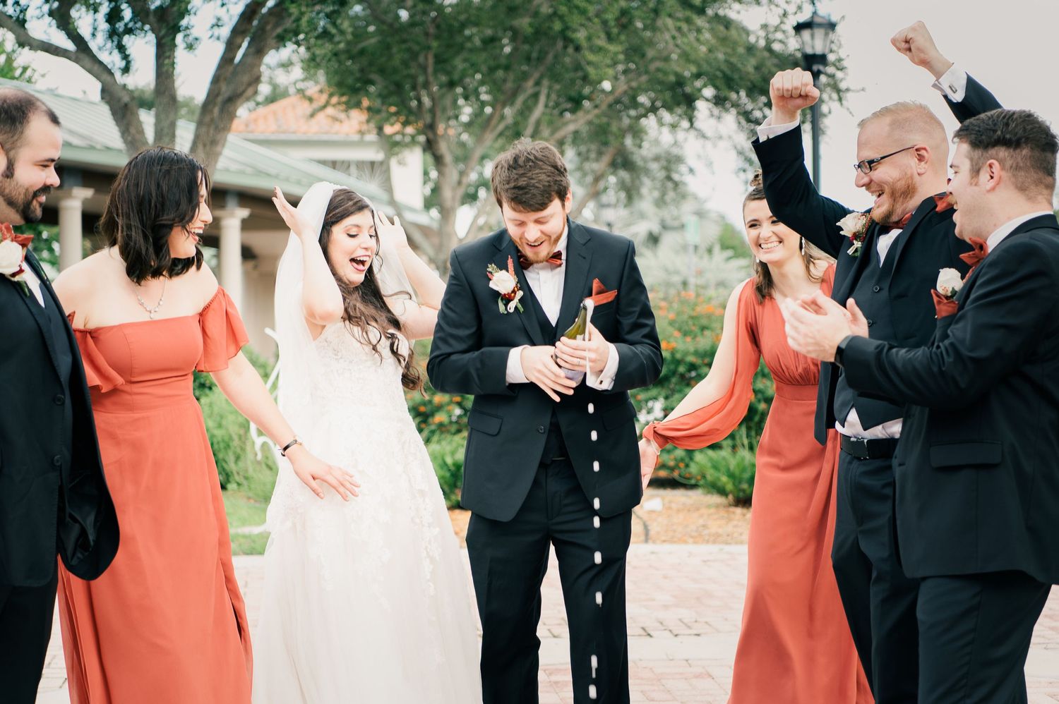 Wedding party celebrates with joy as confetti falls in outdoor ceremony setting.