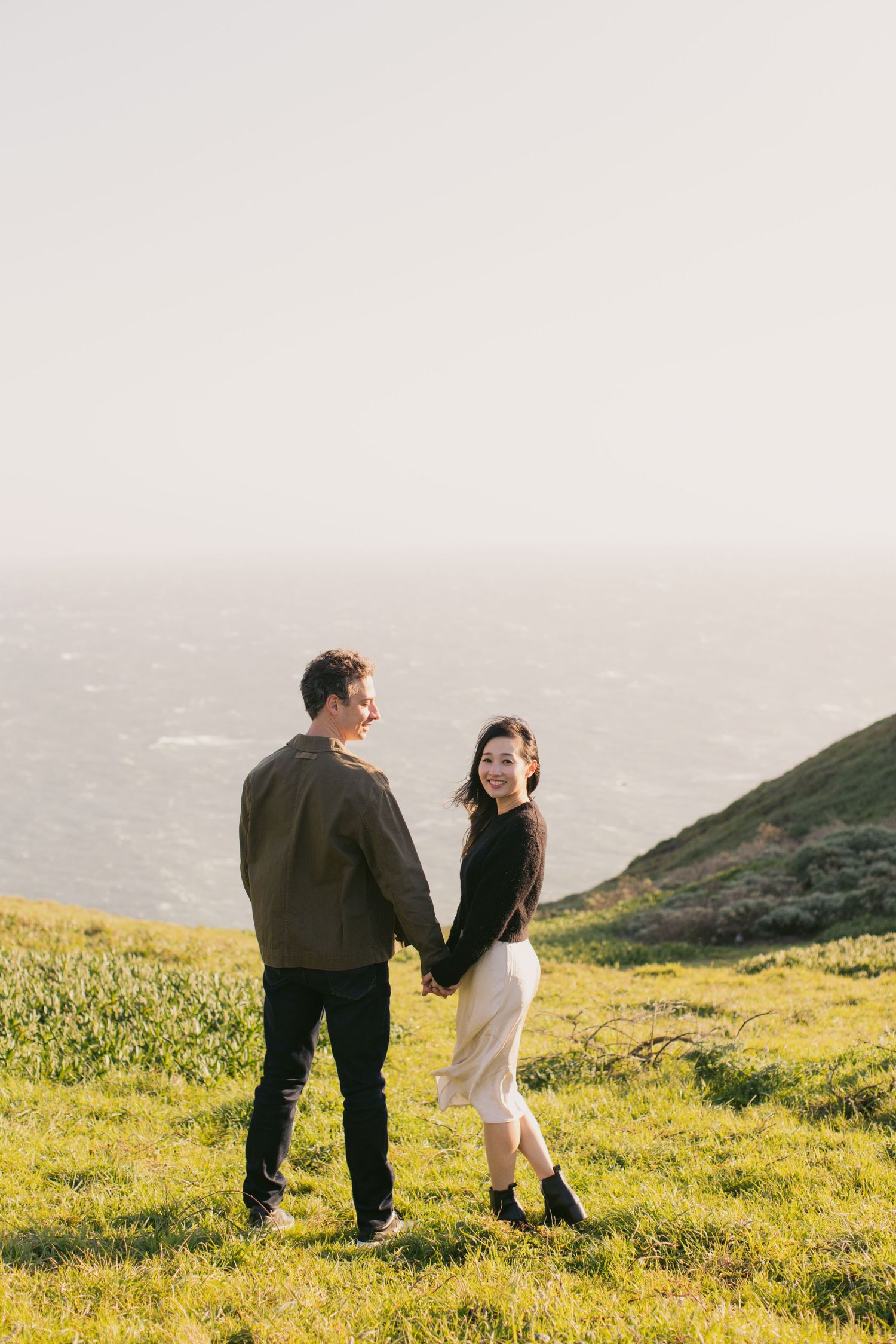 Couple walking hand in hand on a scenic hillside path with ocean views.