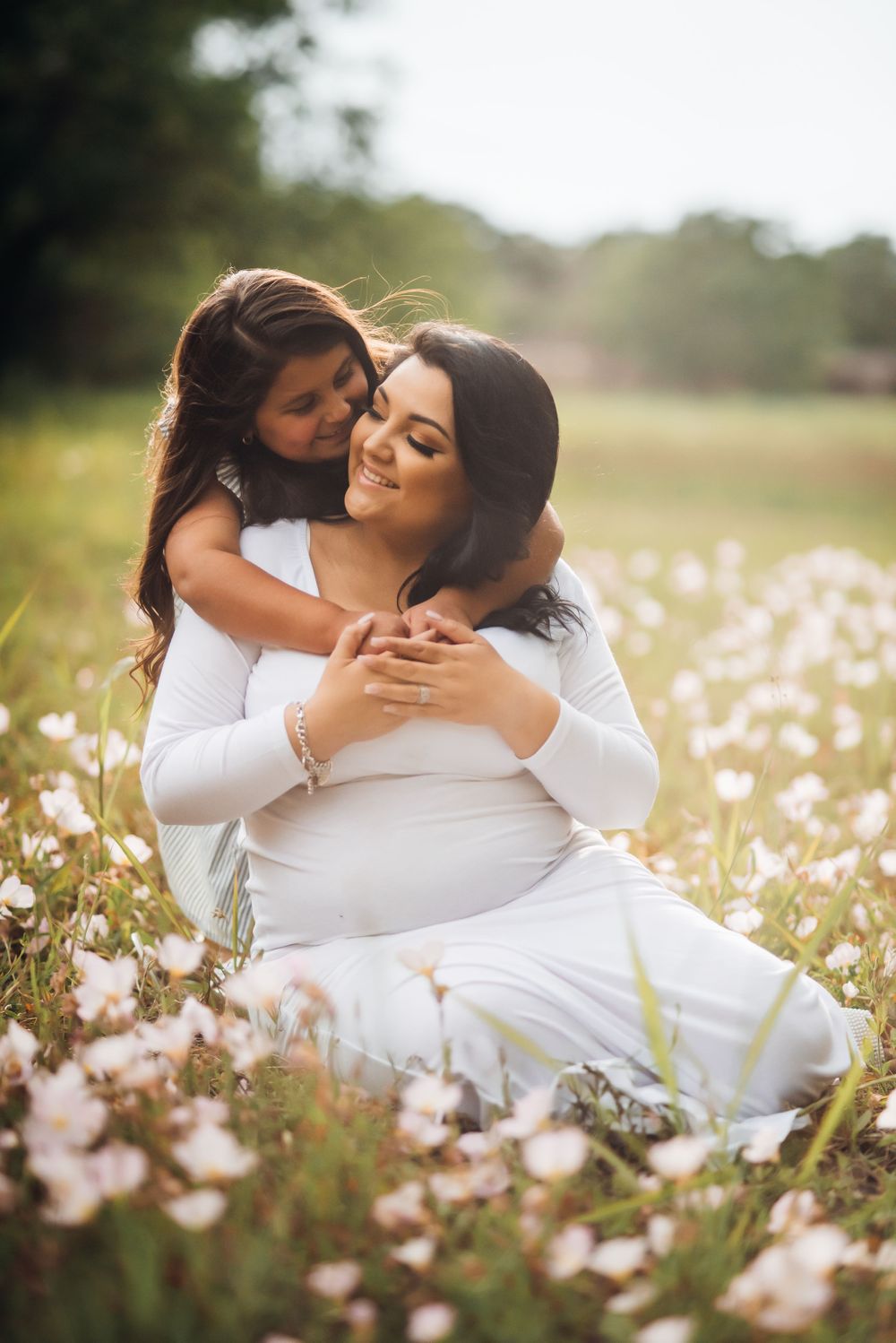 A tender embrace shared between two people in white dresses amid a field of wildflowers.