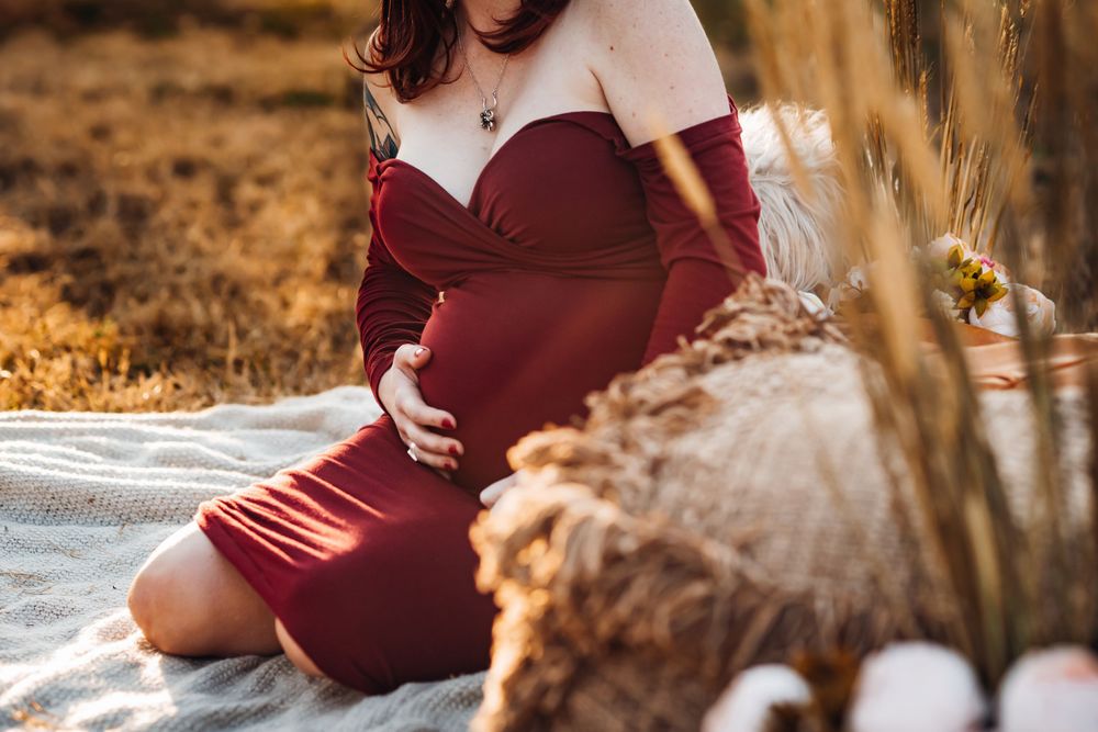 Close-up maternity photo with burgundy dress and rustic decor elements.
