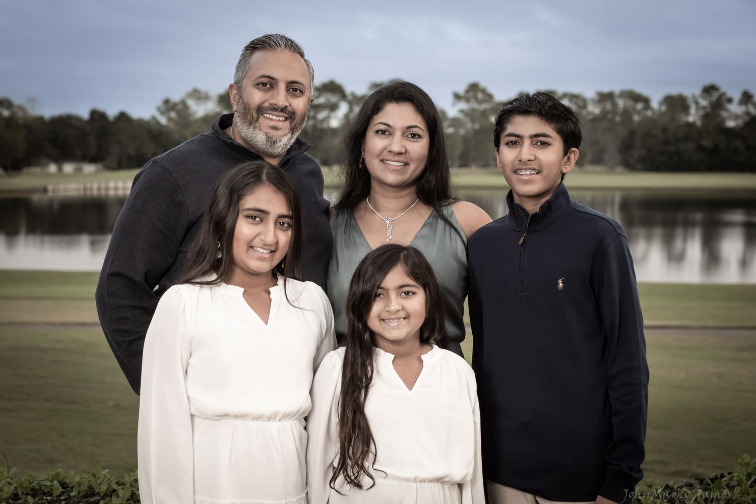 A lakeside family portrait captured outdoors on a cloudy day with water in the background.