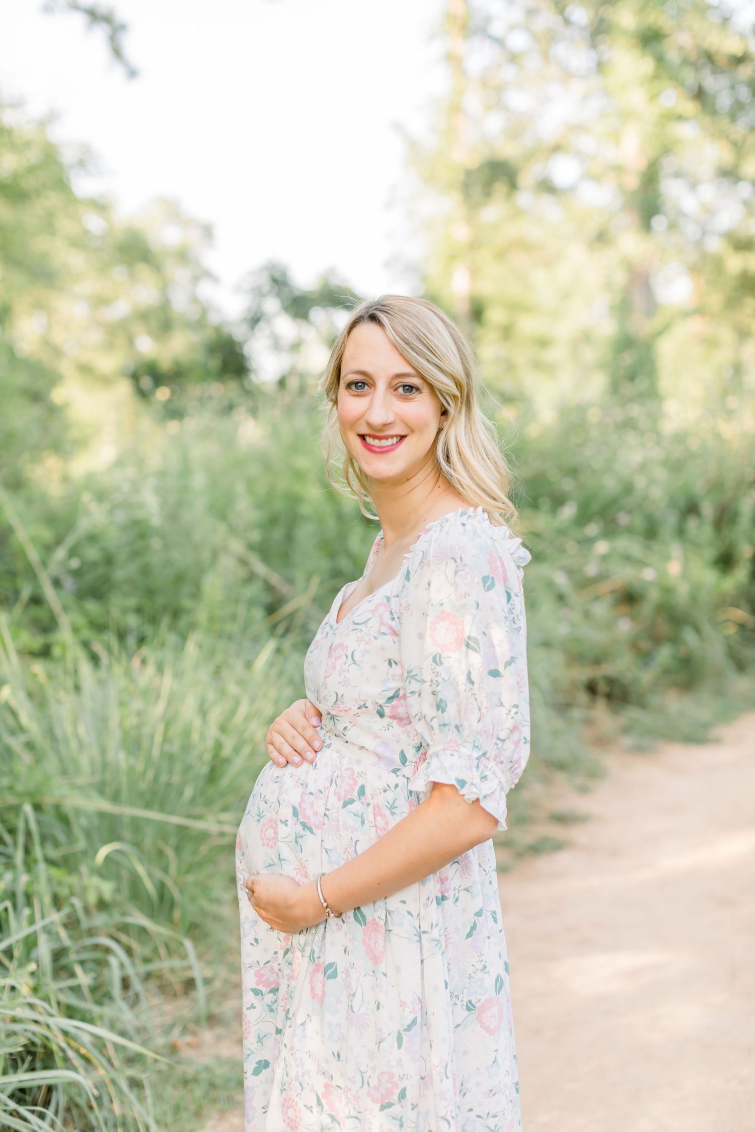 Joyful maternity moment captured on nature path in feminine floral dress.