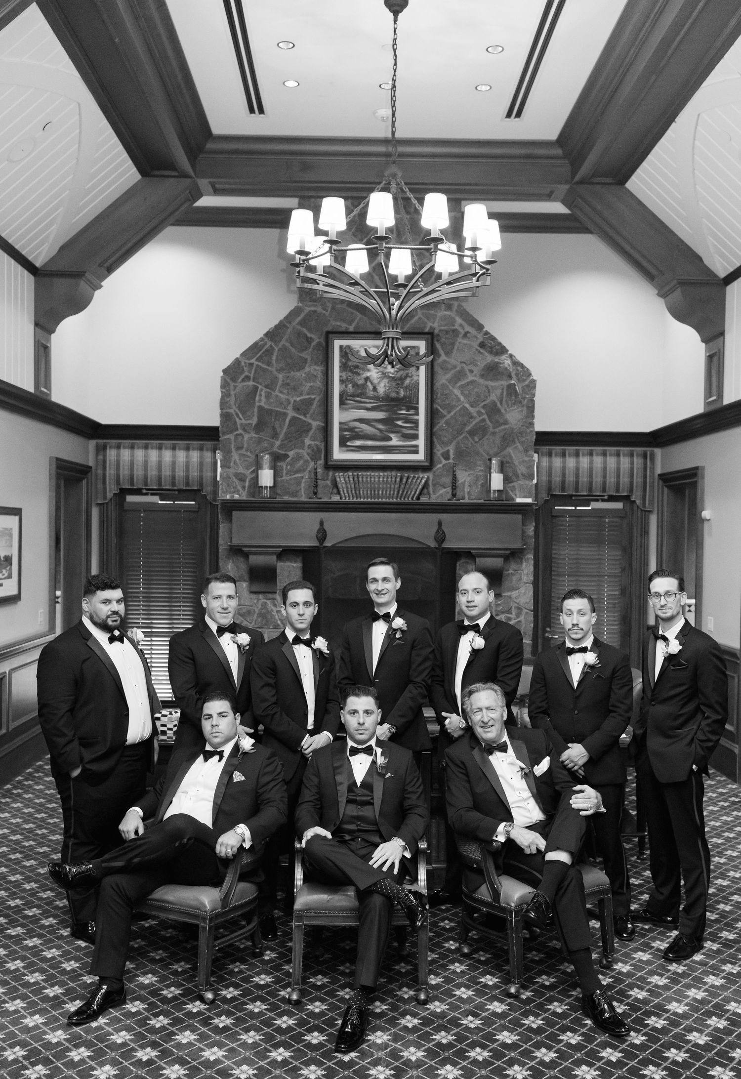 Formal groomsmen group portrait in elegant wood-paneled room with chandelier.