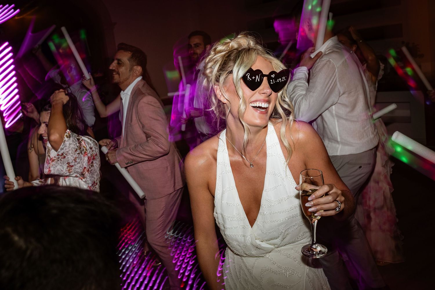 Person in white dress dances at a party with glowing neon lights and holding a wine glass in hand at Quinta da bichinha