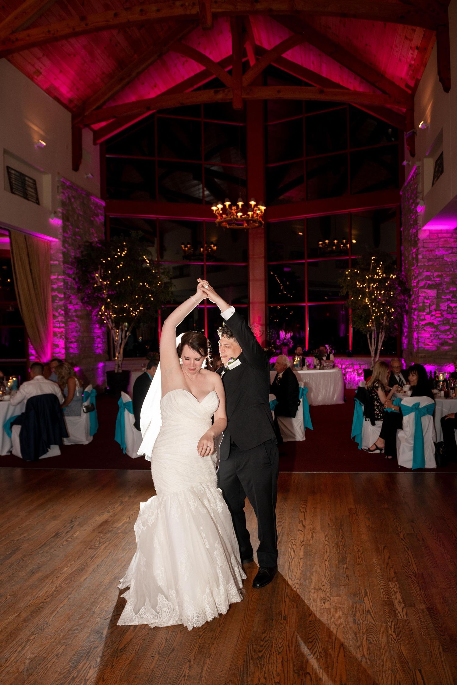Couples dancing on wooden floor under dramatic pink lighting at wedding reception.