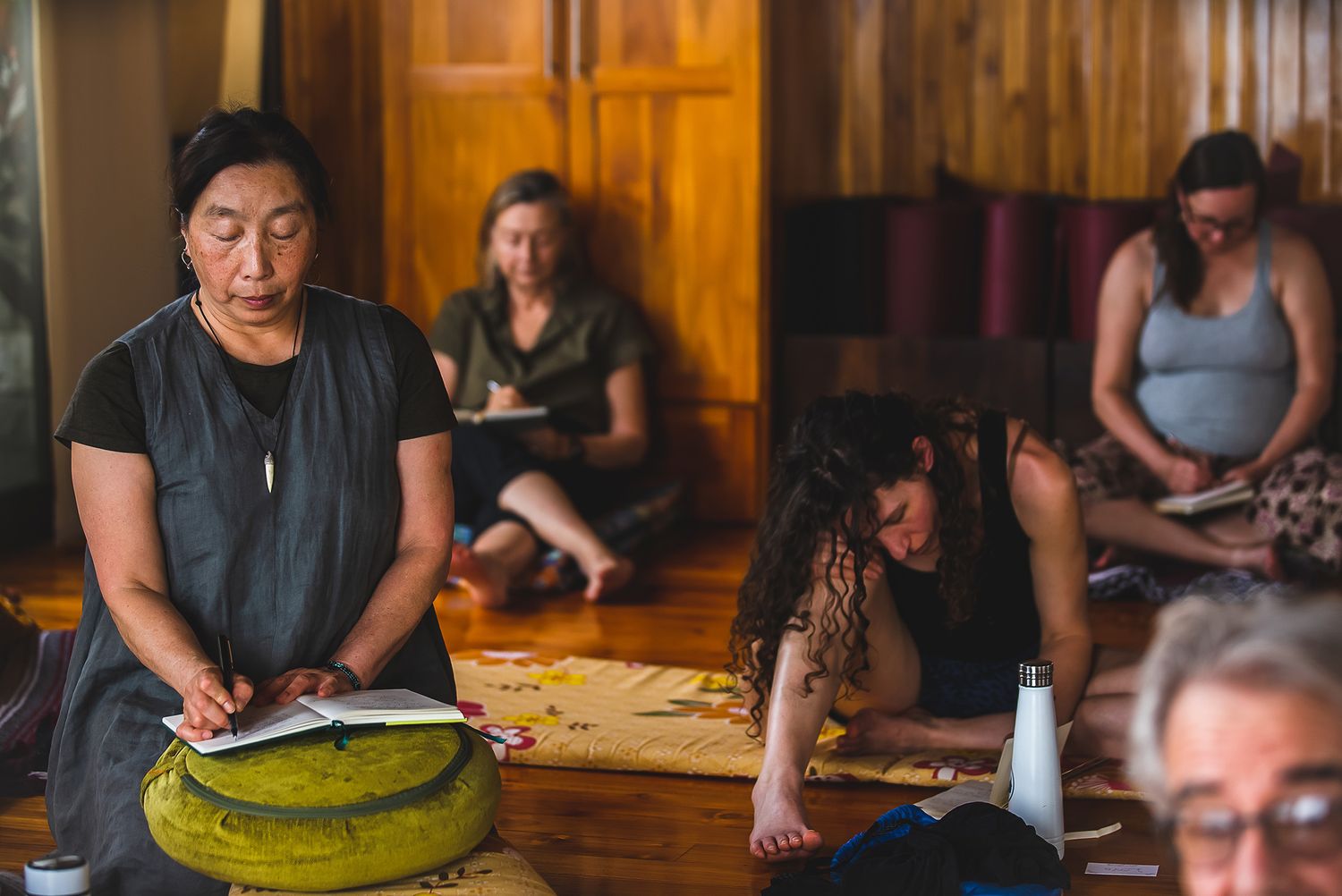 Workshop participants gather around traditional drums in wooden-floored studio space.