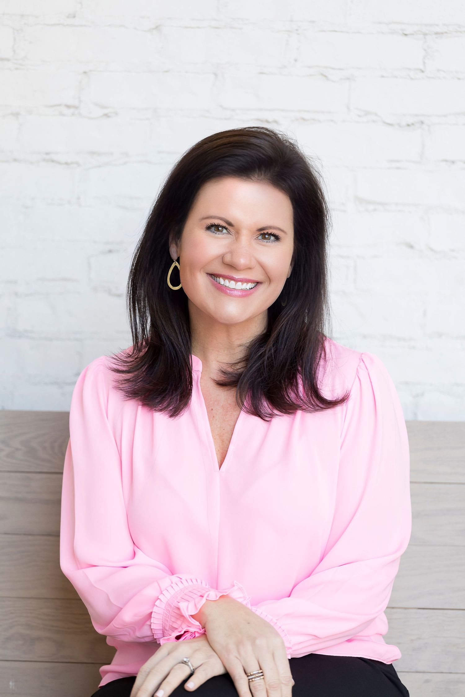 professional headshot of woman sitting on a bench with white brick background by Carter Photography & Design