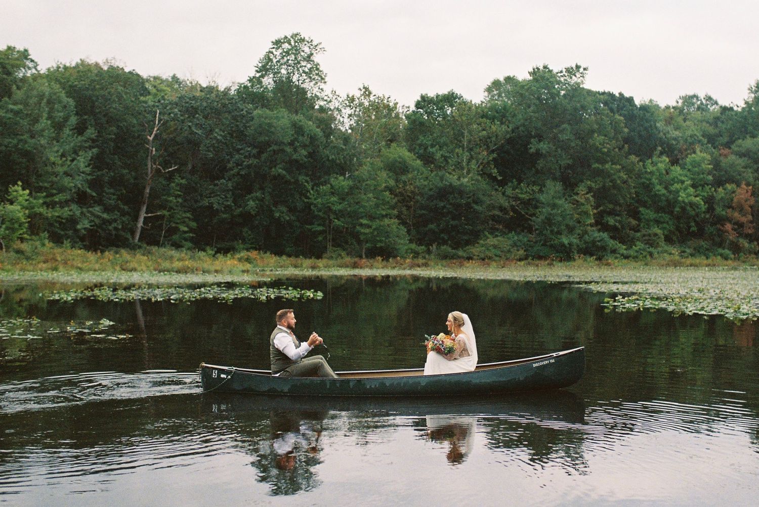 Wedding couple enjoying a peaceful day on rowboats in a serene lake surrounded by trees.