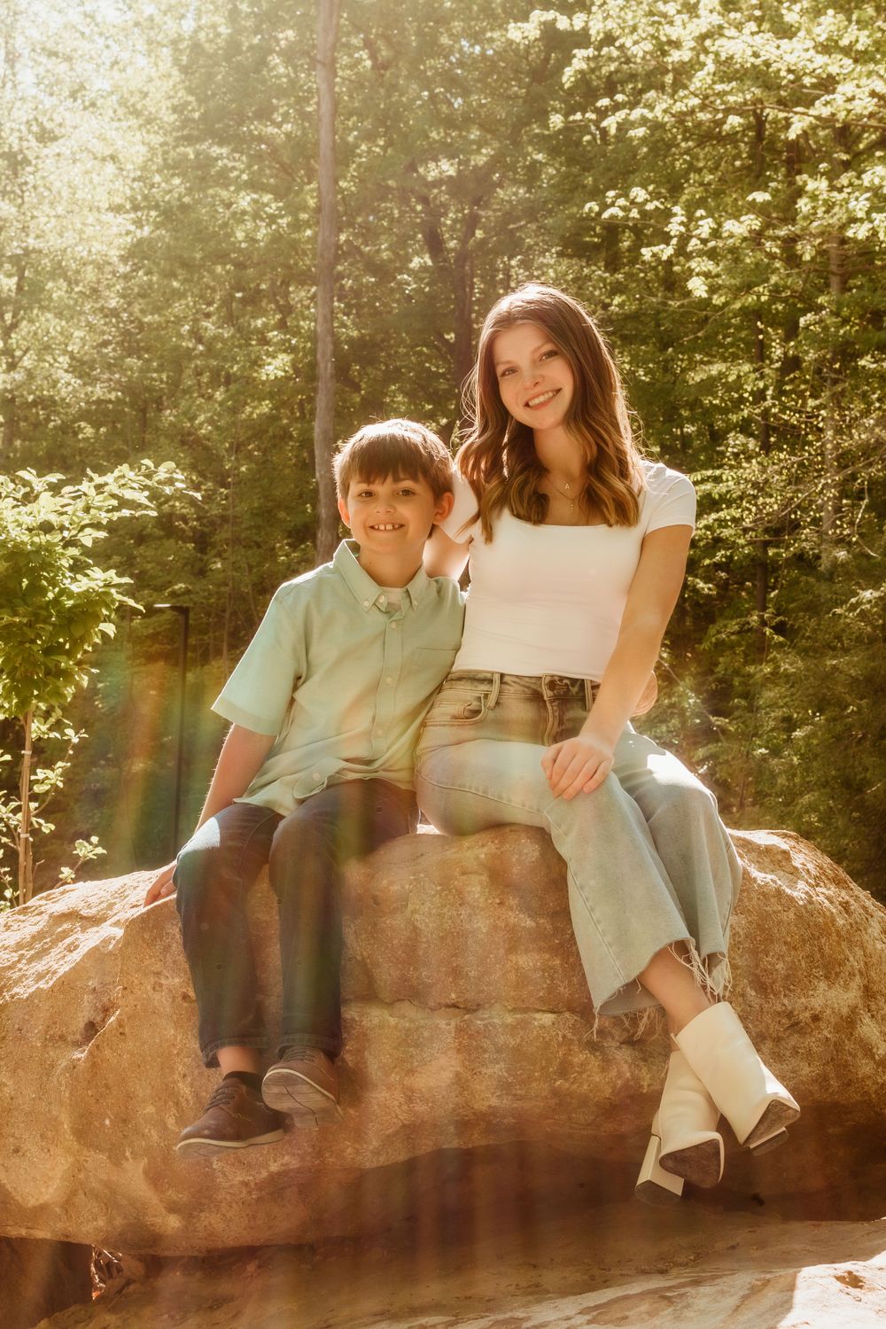 A tender outdoor family photoshoot on a large rock in a sunlit wooded area.