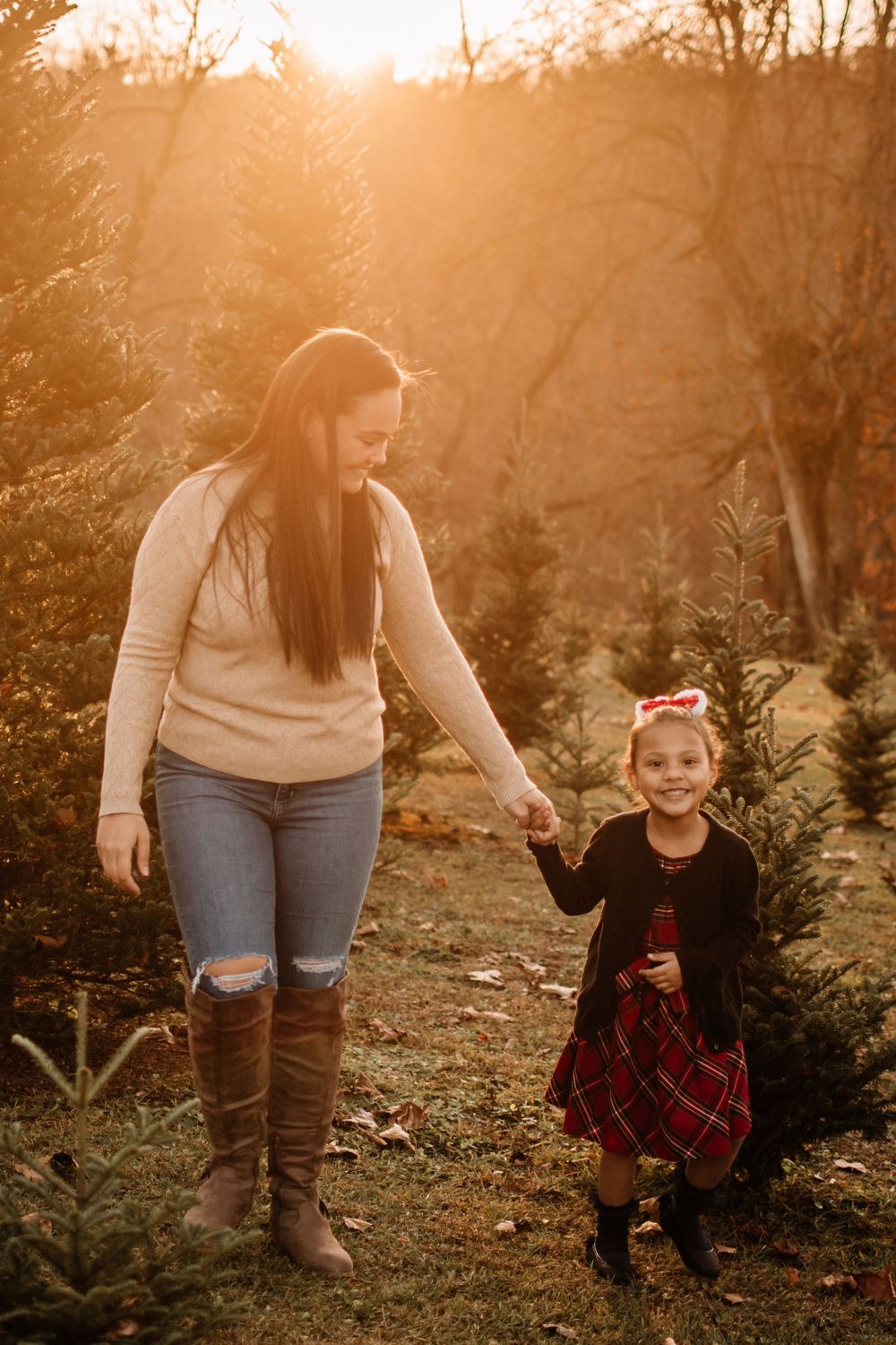 Parent and child hold hands while walking through Christmas tree farm at sunset.