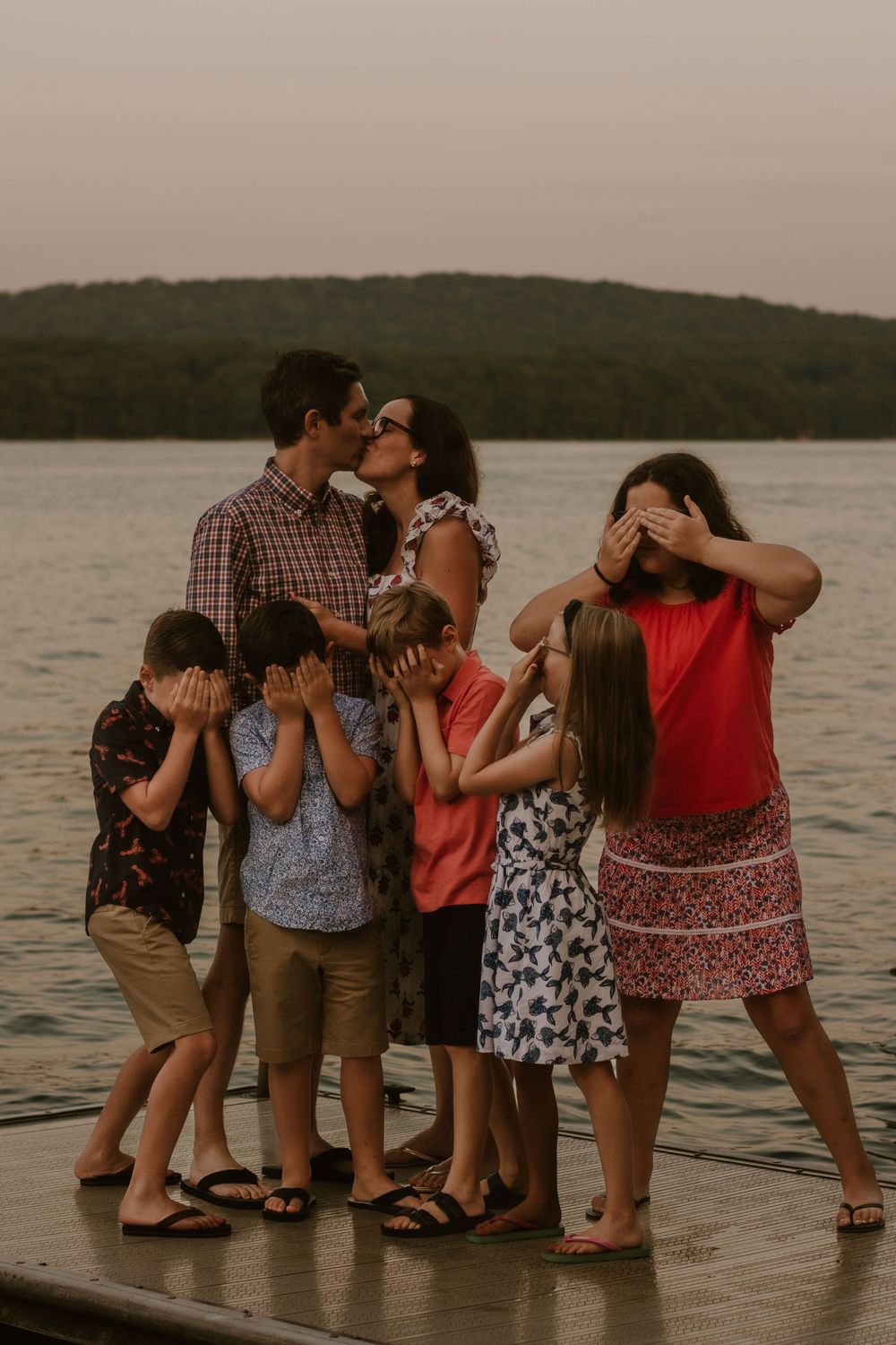 Group stands together in shallow water at sunset creating playful poses on dock.