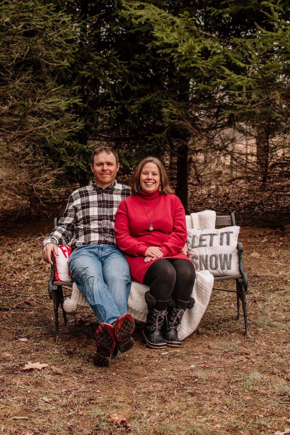 Couple sitting on outdoor bench during winter photo session with festive signs.