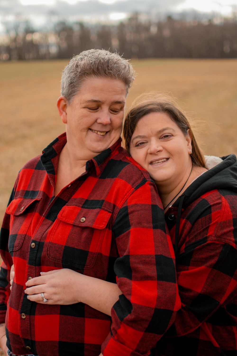 Two people in matching red buffalo plaid shirts share intimate moments in a field.