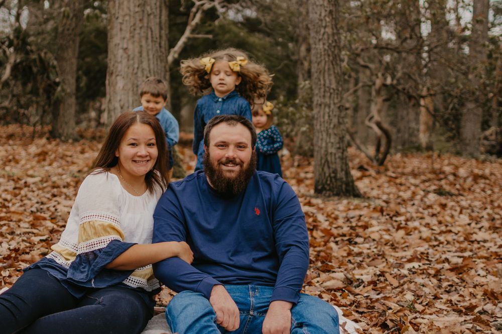 Family photo session in a forest with fallen autumn leaves showing joyful candid moments.