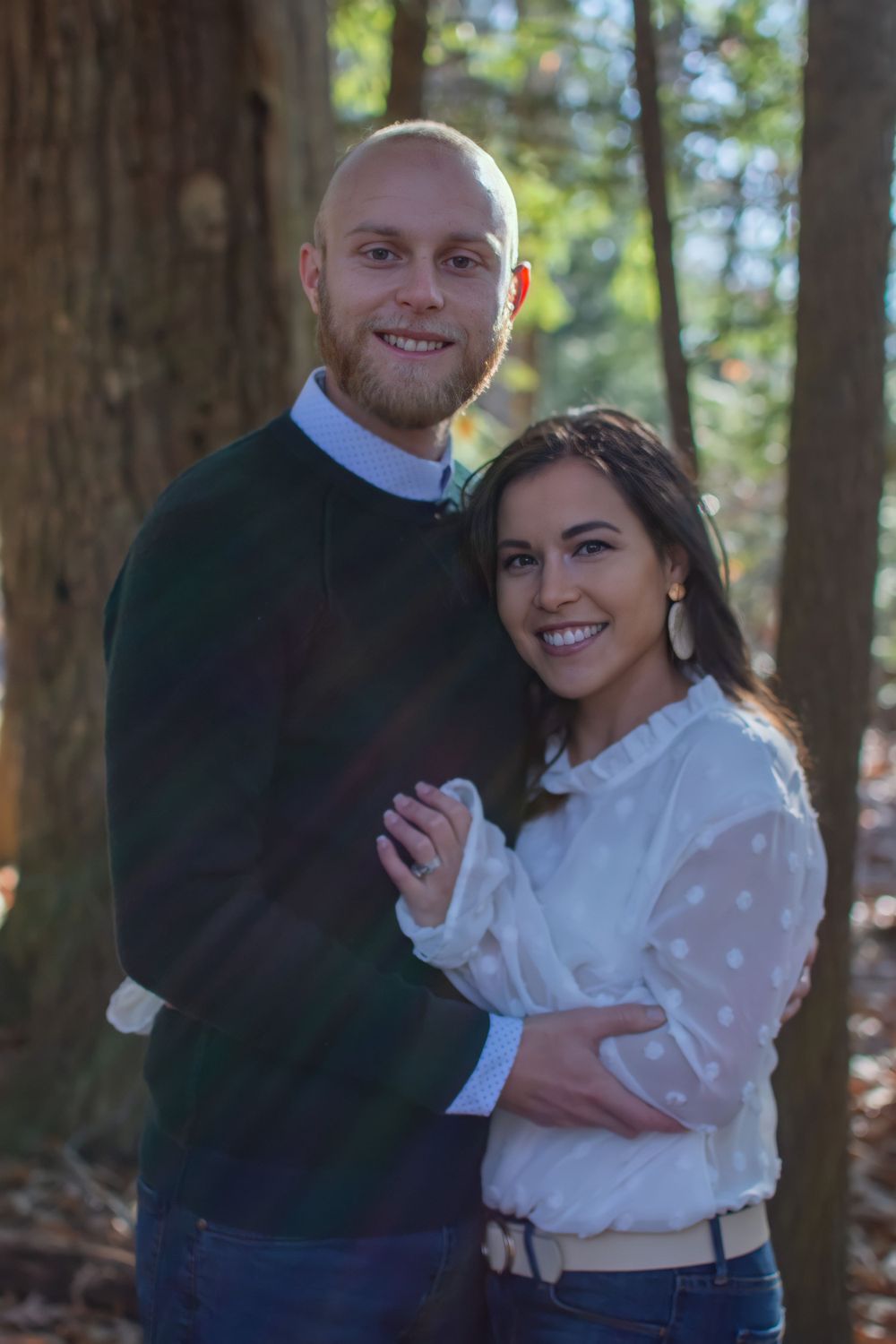 A couple poses together in a forest setting wearing coordinated white and navy outfits.