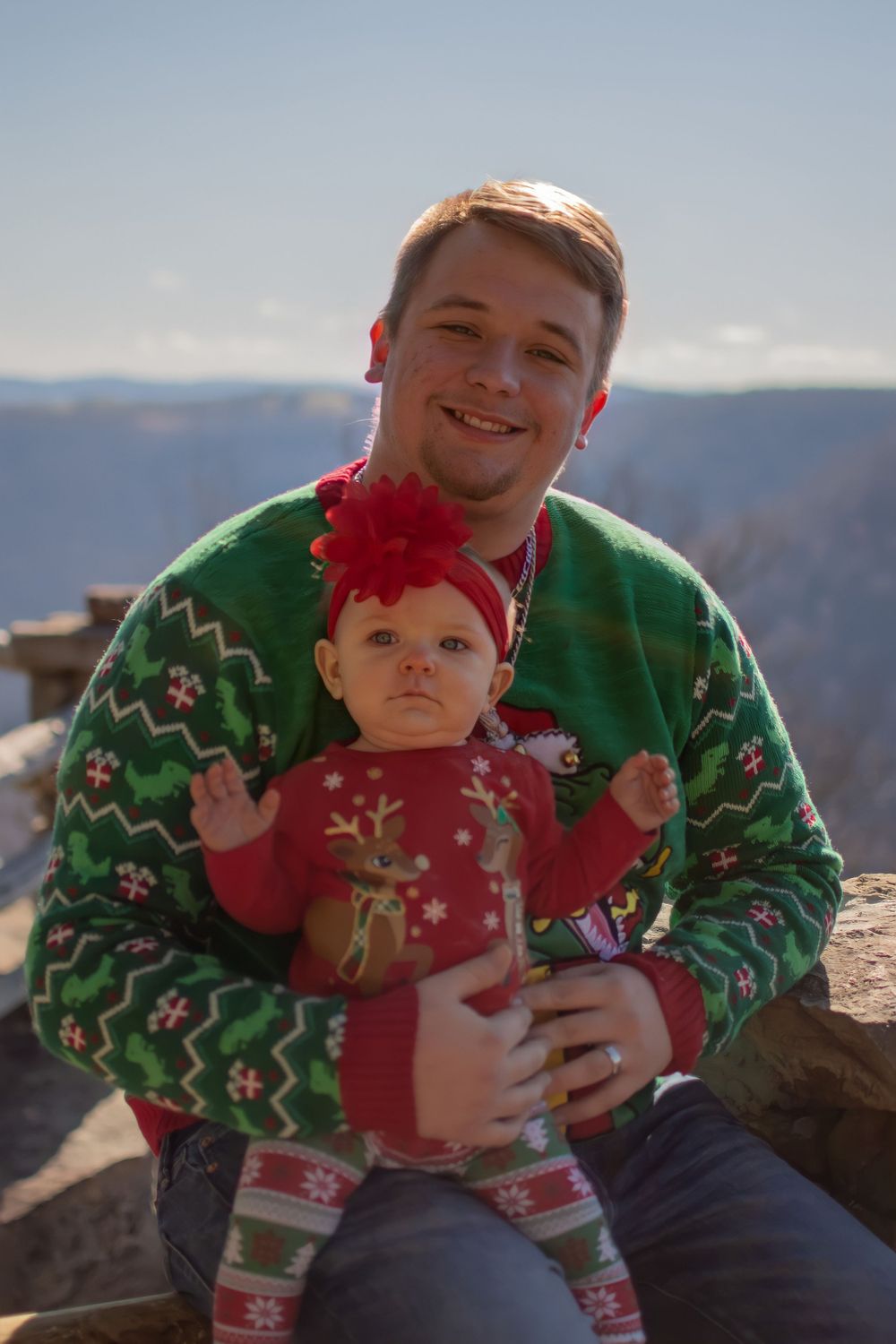 Holiday portrait featuring matching Christmas sweaters against a mountain backdrop.