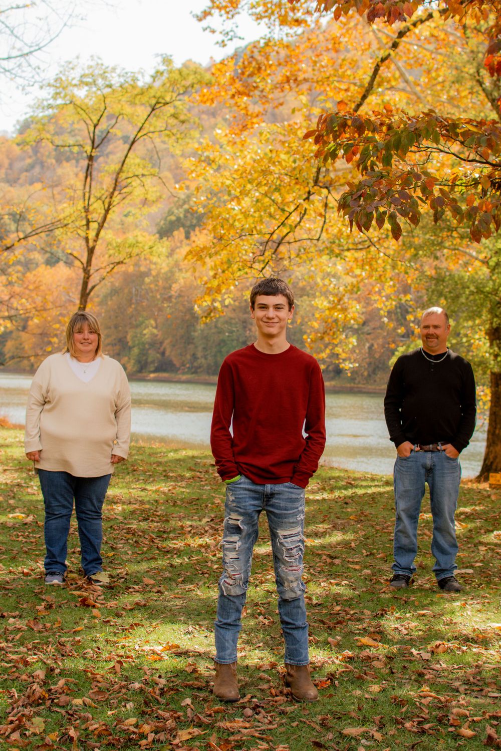 People standing in a line on grass with fall trees and colorful autumn leaves in the background.