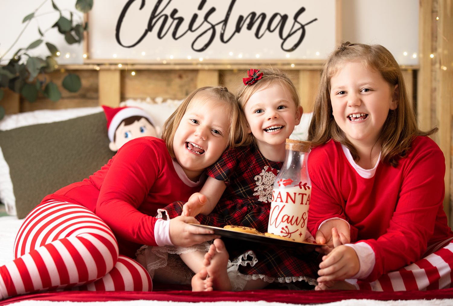 Children in matching red and striped outfits laugh while looking at a tablet during Christmas.