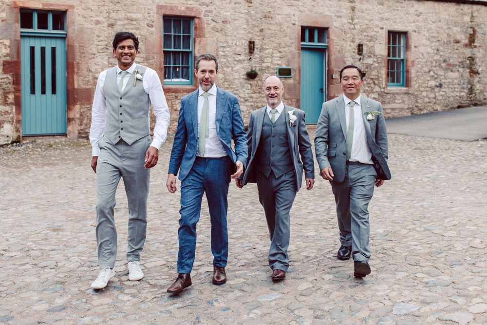 Wedding party members lined up against rustic stone building with teal doors.