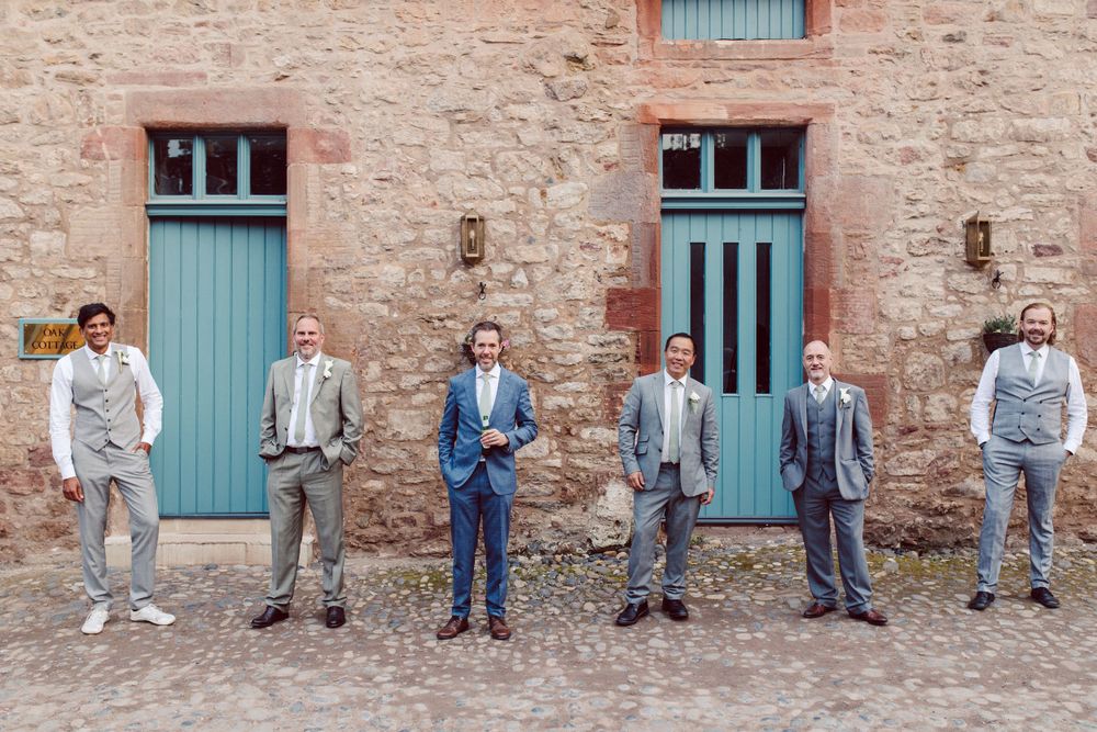 Wedding guests arranged in casual poses along stone wall with turquoise doors.