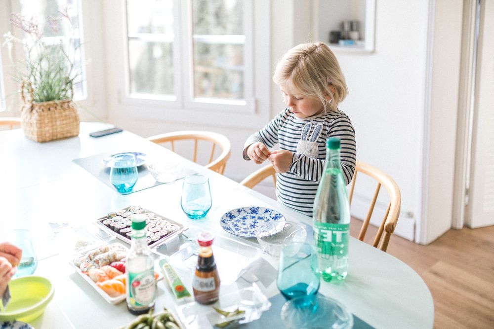 Child enjoying meal at bright dining table set with blue glassware and various dishes.