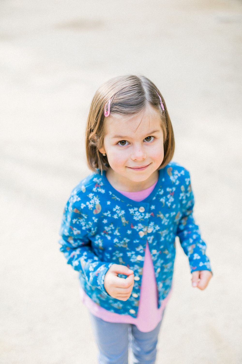 A smiling child wearing a blue floral print sweater and gray pants stands against a light background.