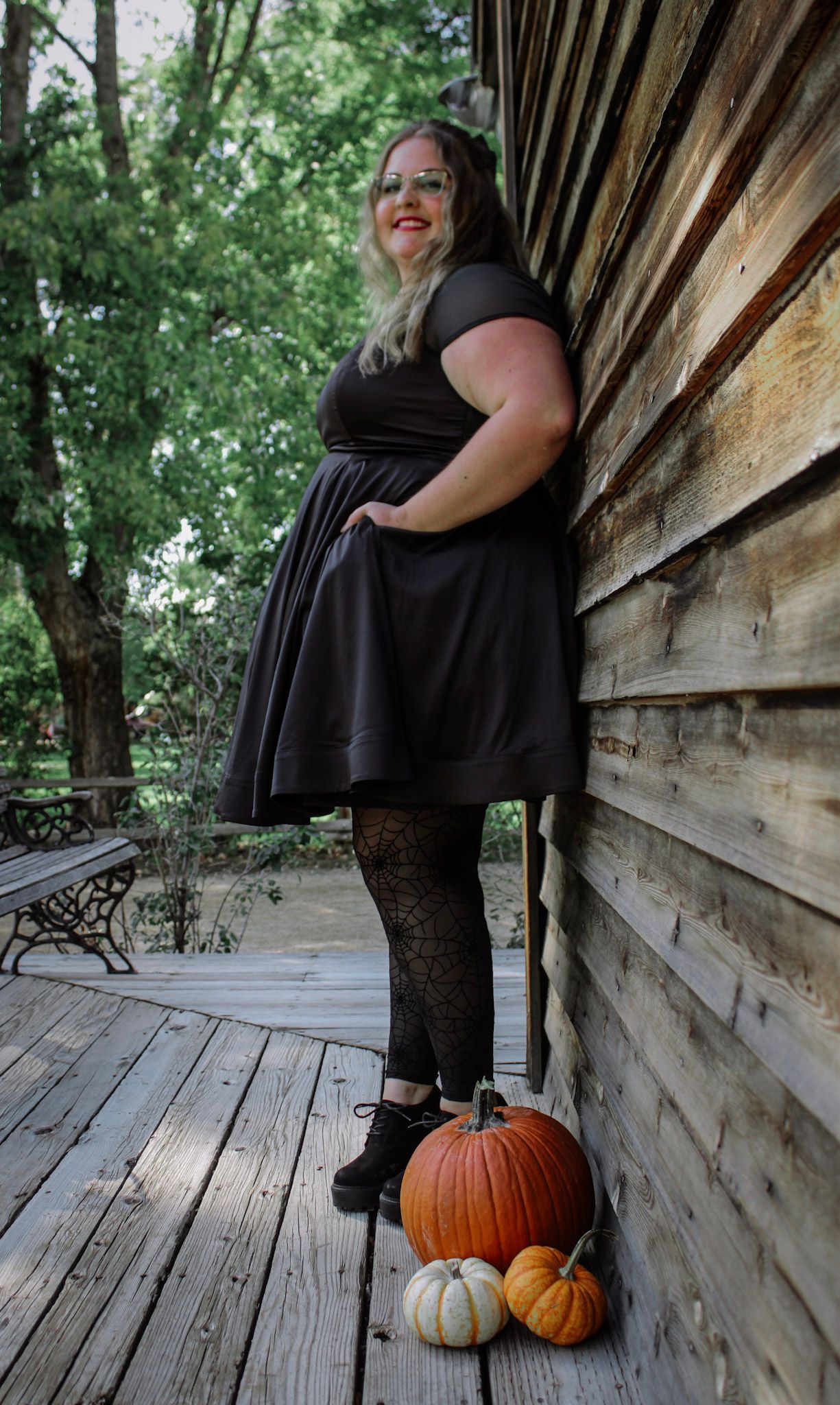 A fall fashion photoshoot with black dress, patterned tights, and decorative pumpkins on a wooden deck.