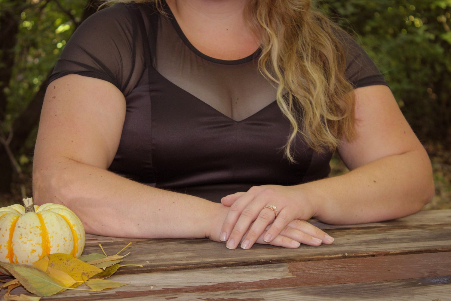 Close-up fashion detail of black mesh dress with decorative pumpkin on rustic wooden surface.