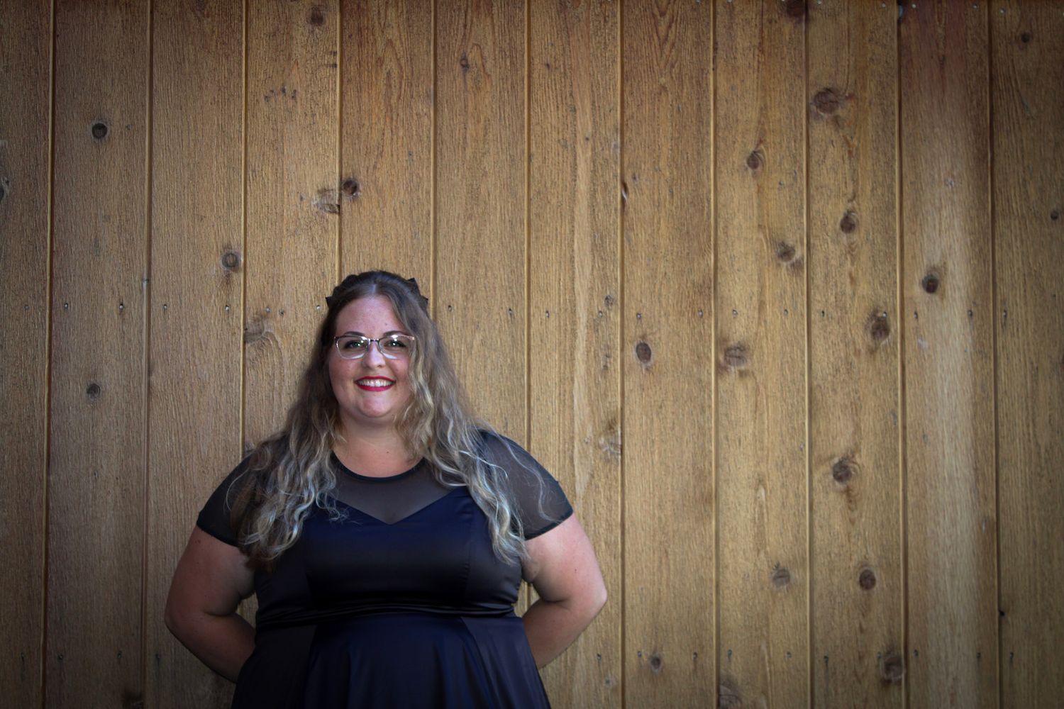 Fashion portrait against wooden paneled wall wearing black dress.