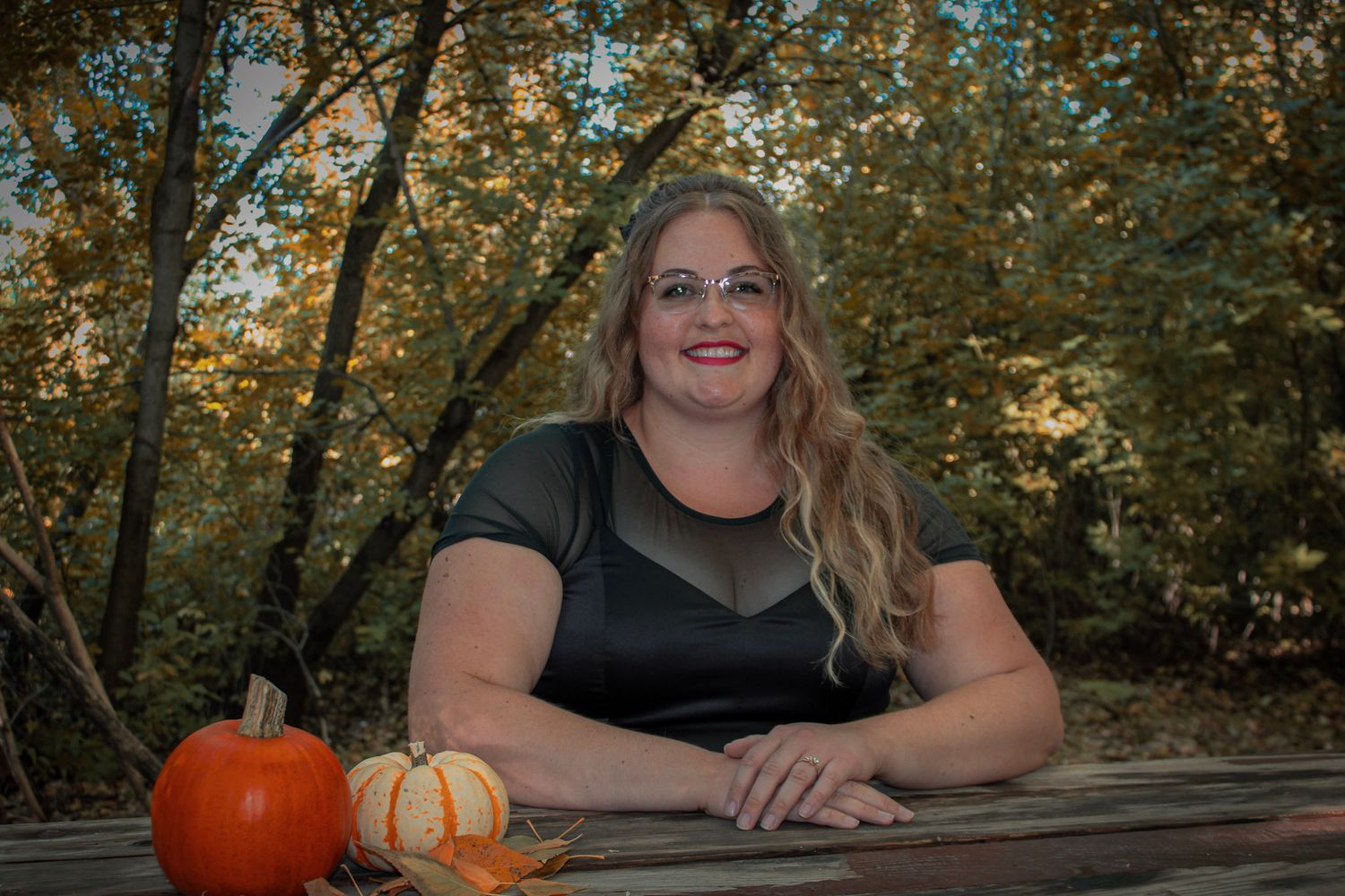 Autumn outdoor portrait with pumpkins on wooden table surrounded by fall foliage.