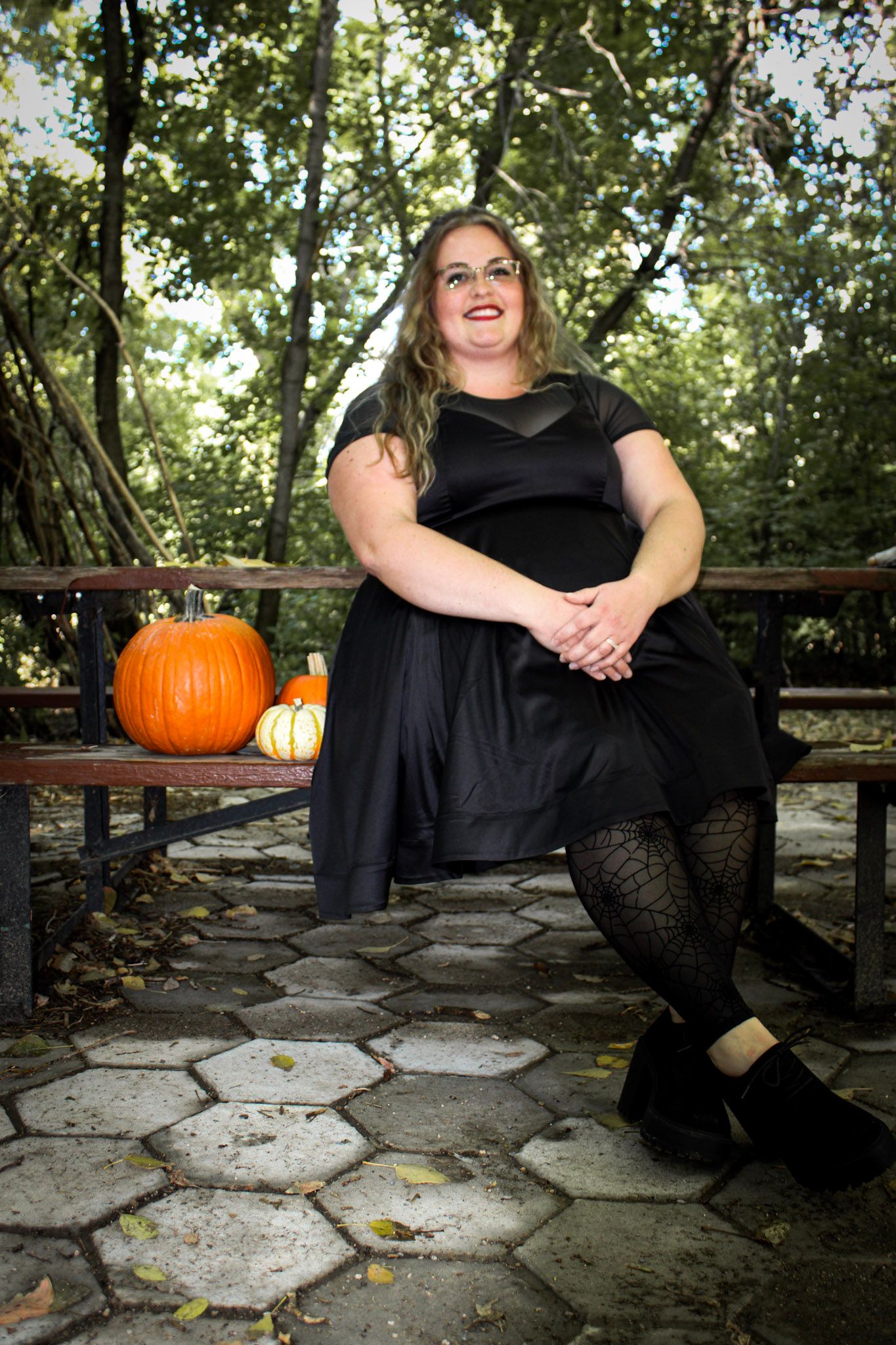 Outdoor fashion portrait on stone path with fall pumpkin decorations and black dress.