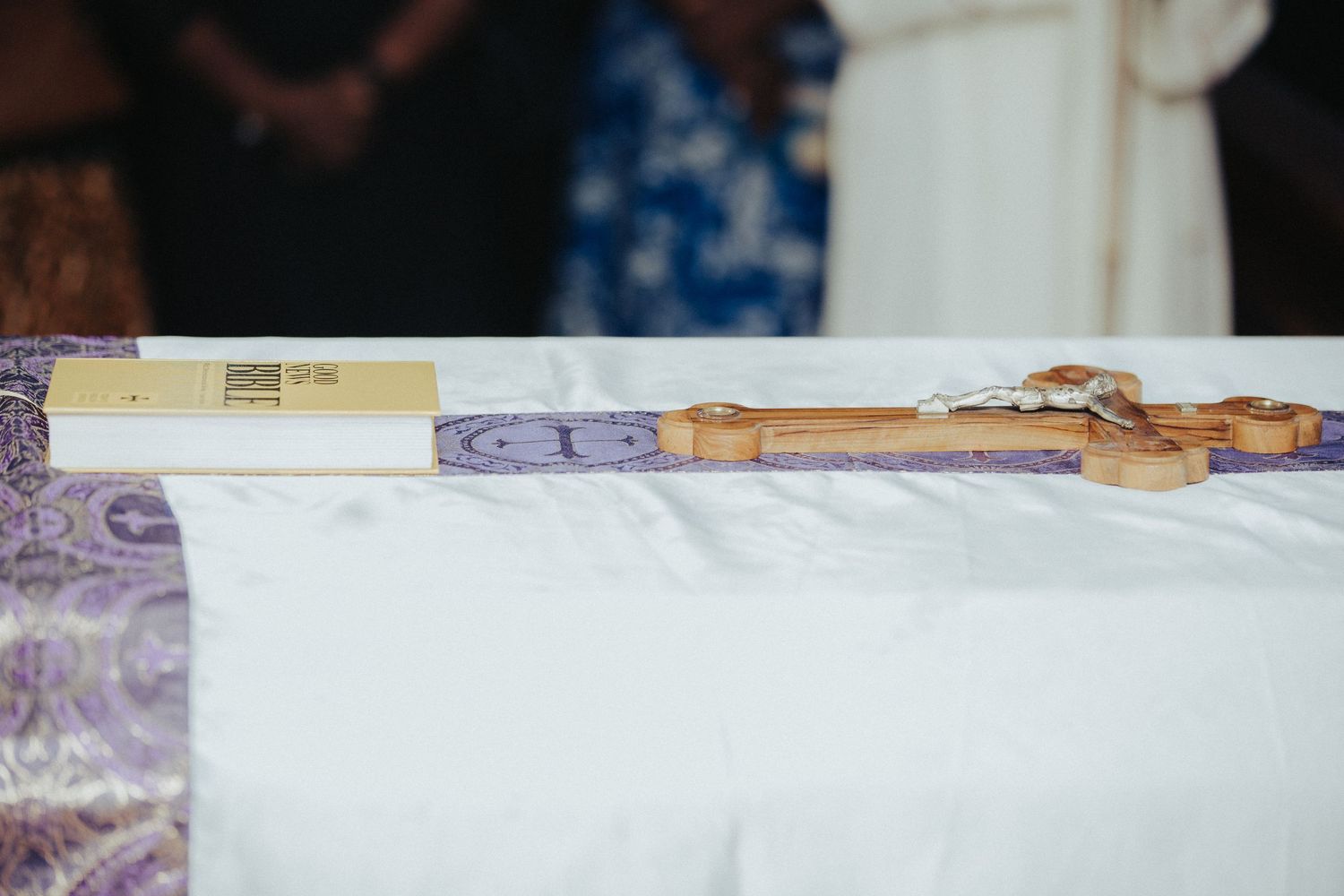 Close-up of a Bible and a wooden cross placed on a white and purple altar cloth.
