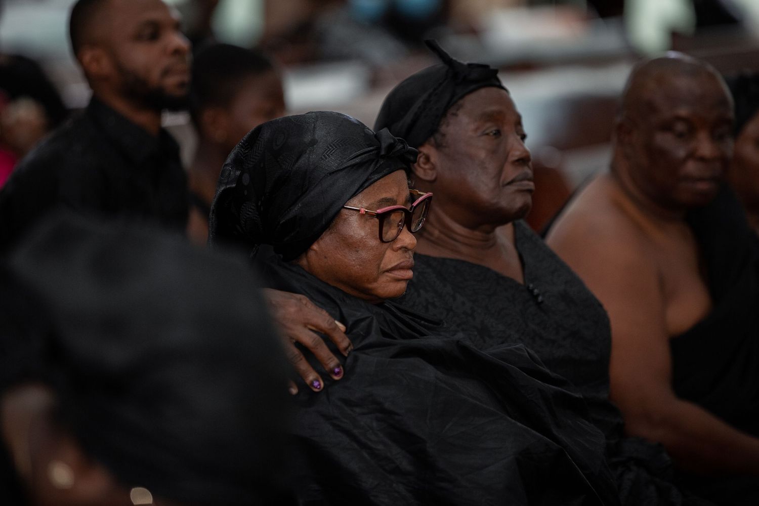 Woman in traditional black mourning cloth and headwrap seated in a church pew.