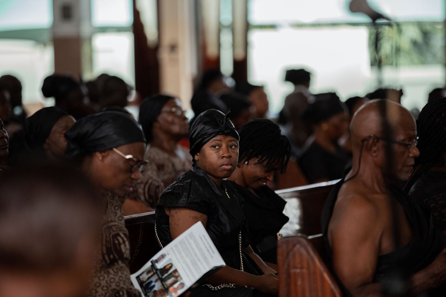 Group of mourners gathered around a white casket during a solemn indoor funeral ceremony.