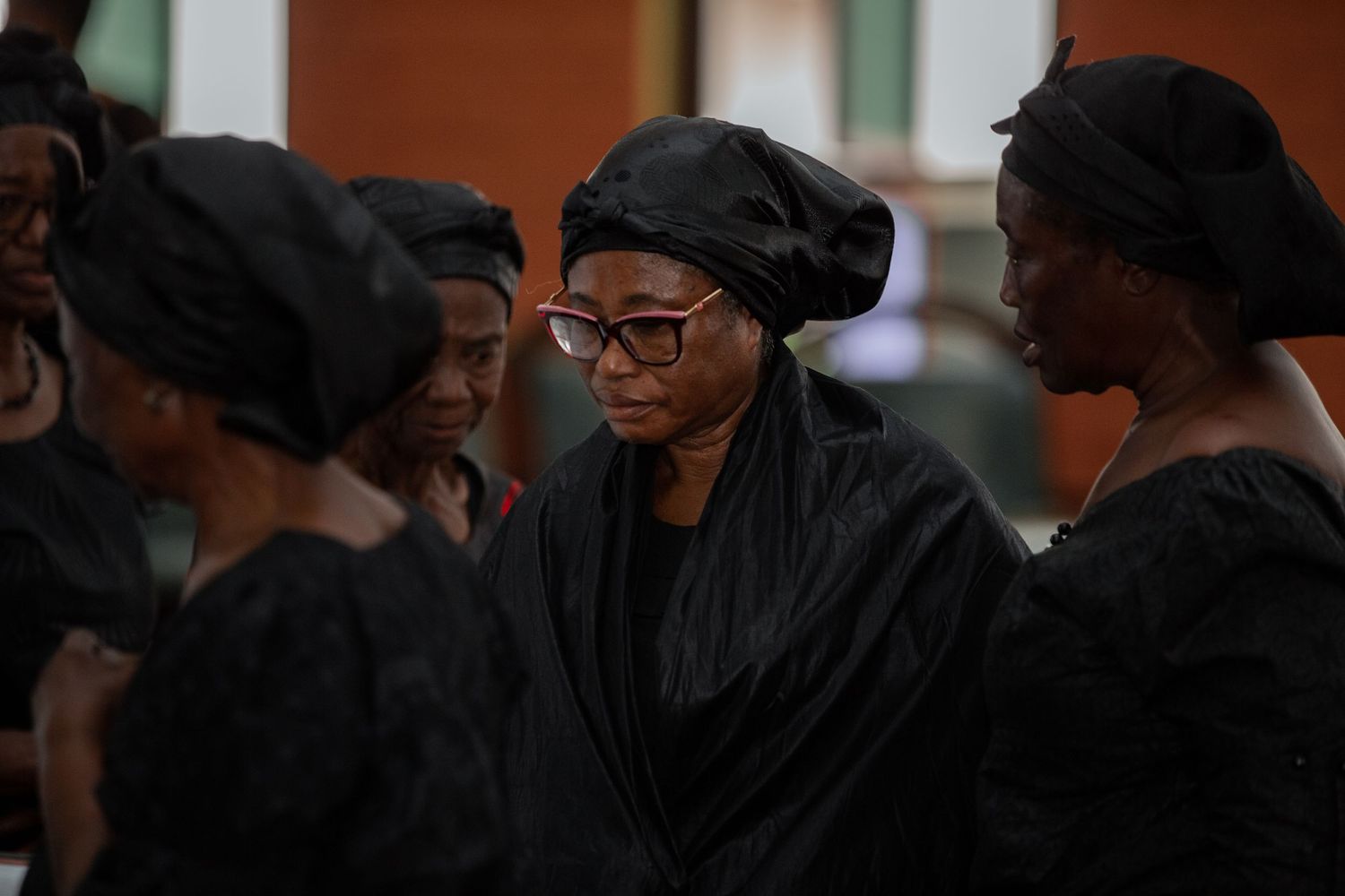 Close-up of family members in black funeral attire standing together in a moment of reflection.