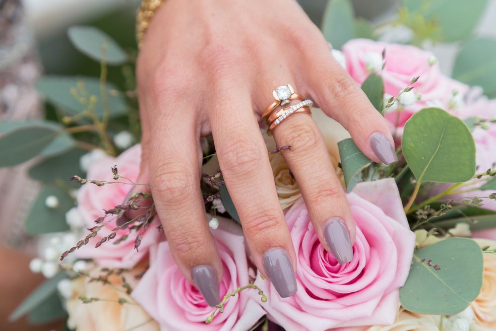 Wedding rings displayed on hand with pink roses and eucalyptus bouquet.