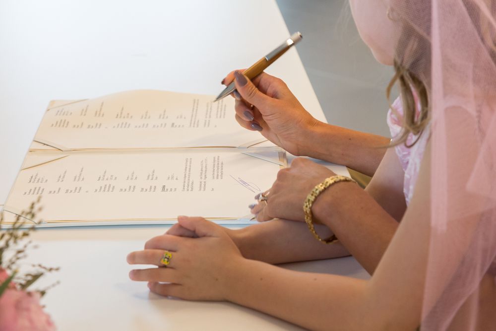 Person in bridal veil signing wedding documents with a pen.
