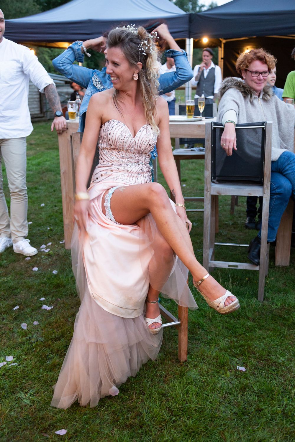 A person in a blush pink sequined gown sits on a chair during an outdoor evening celebration.
