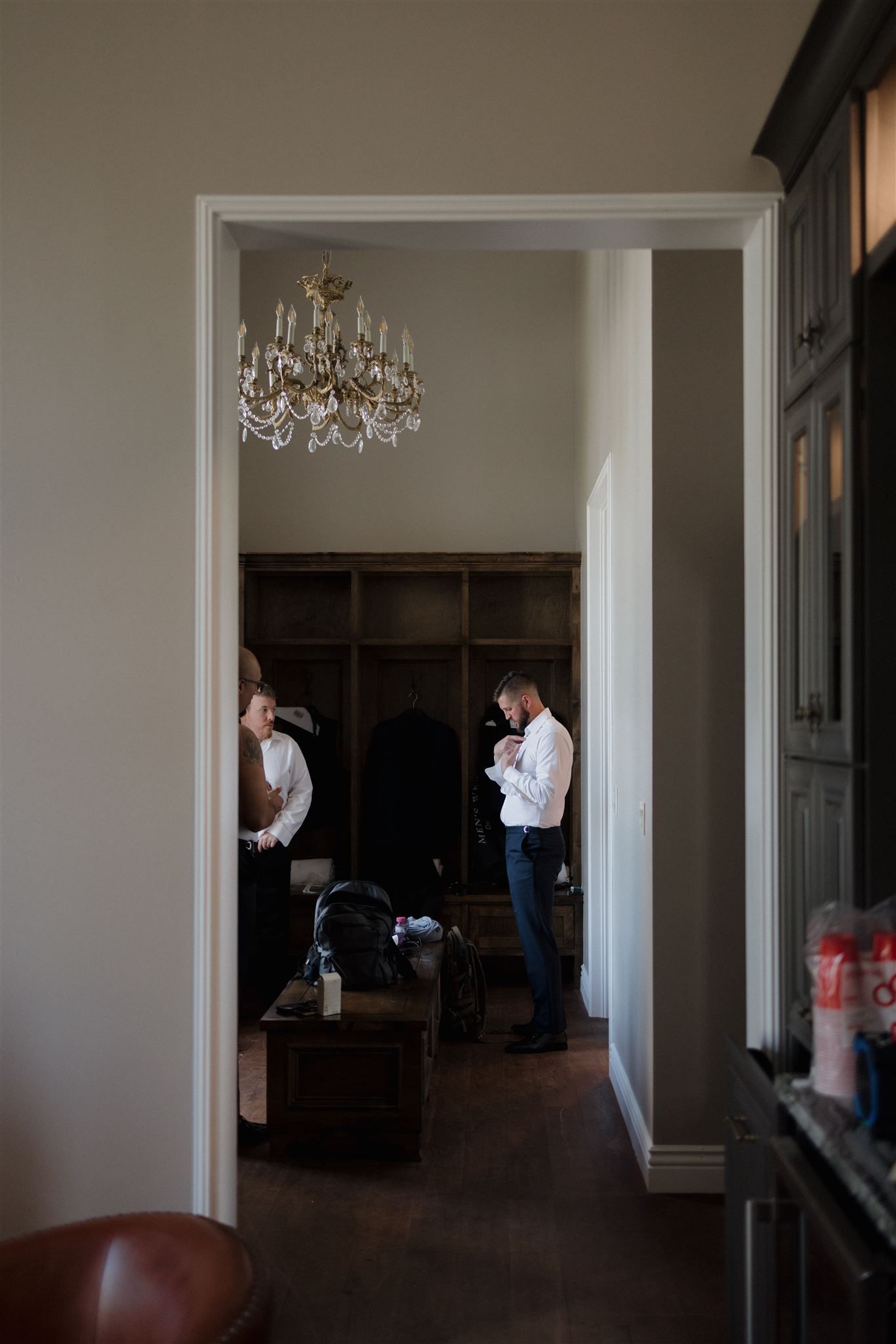 An elegant room interior with a crystal chandelier and dark wood floors is viewed through a doorway.