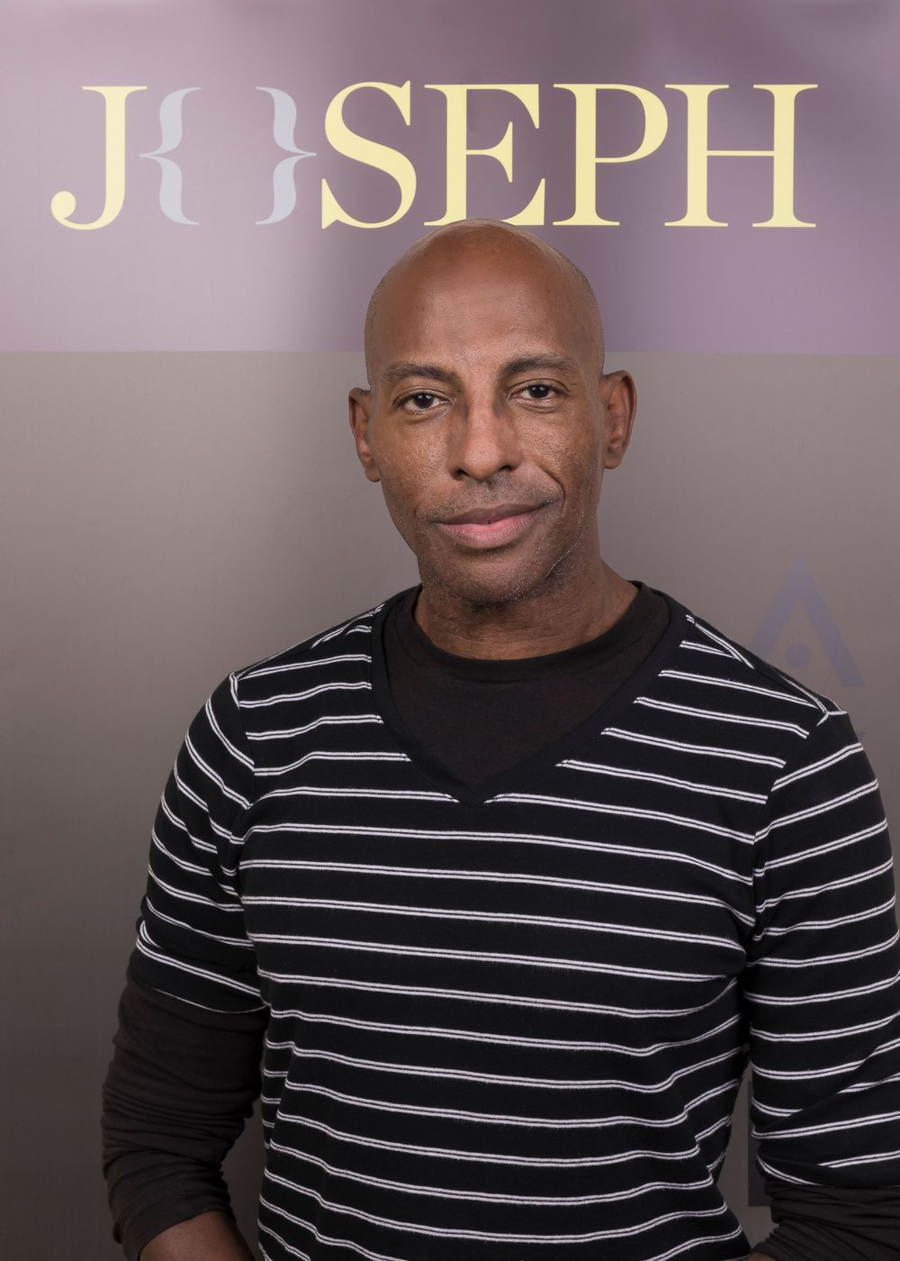 Corporate portrait of a person in a striped sweater against a backdrop with text reading Joseph.