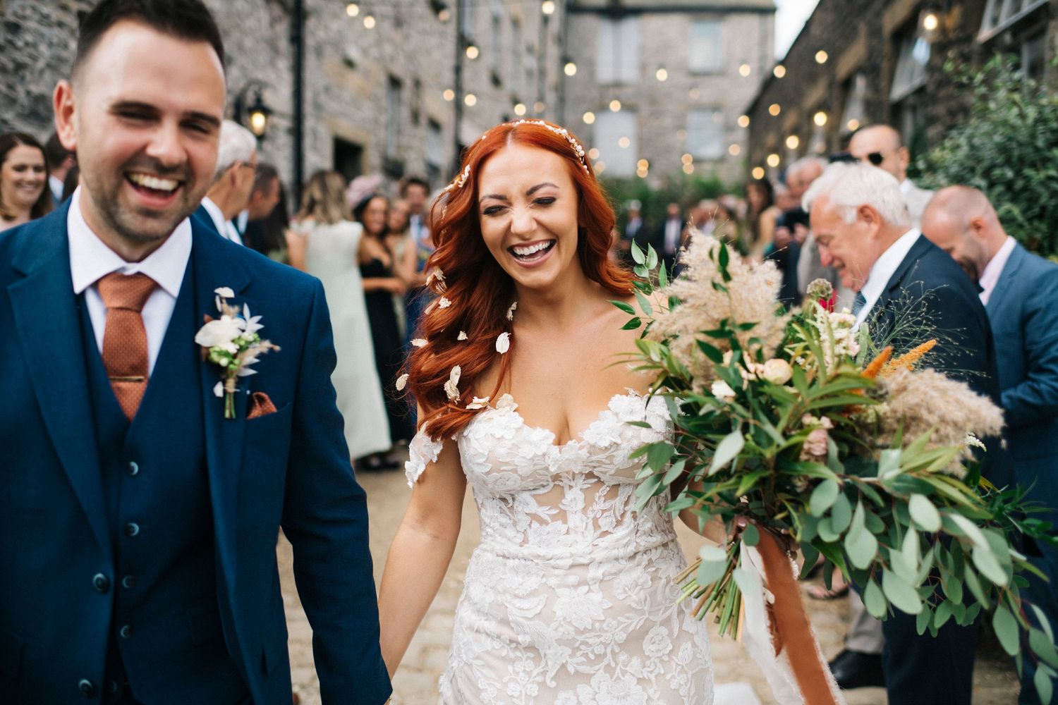 Joyful wedding celebration with couple walking through outdoor venue with lush greenery bouquet.