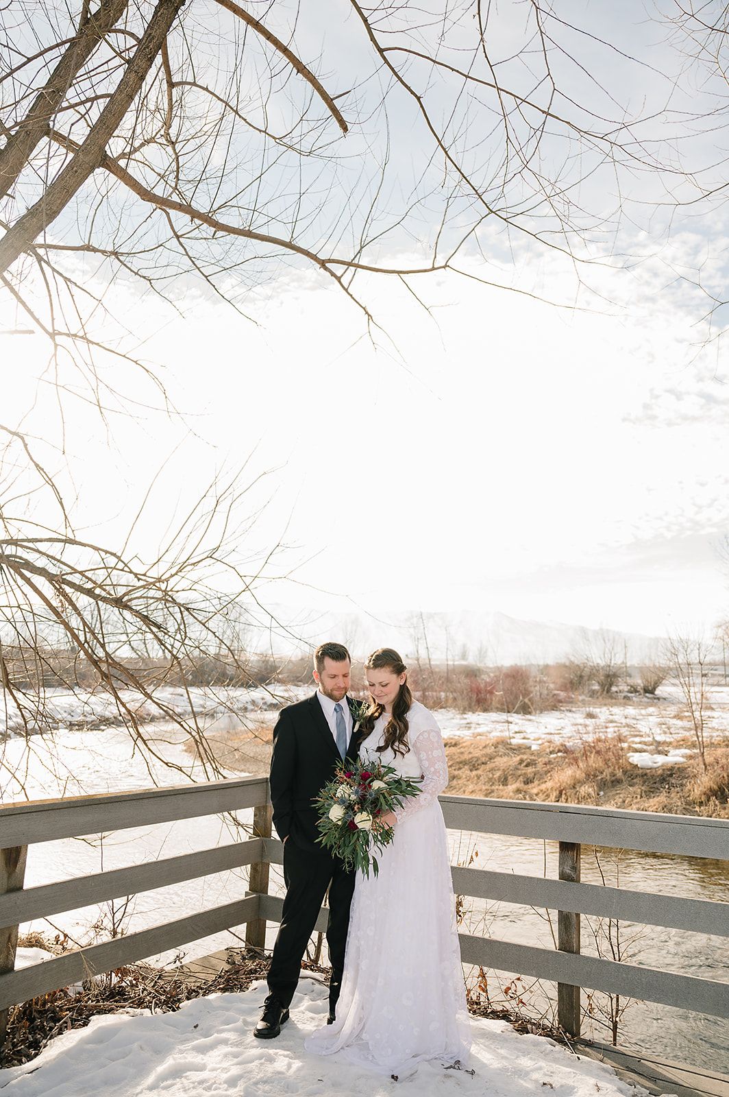 A winter wedding portrait on a wooden bridge with bare trees and snow.