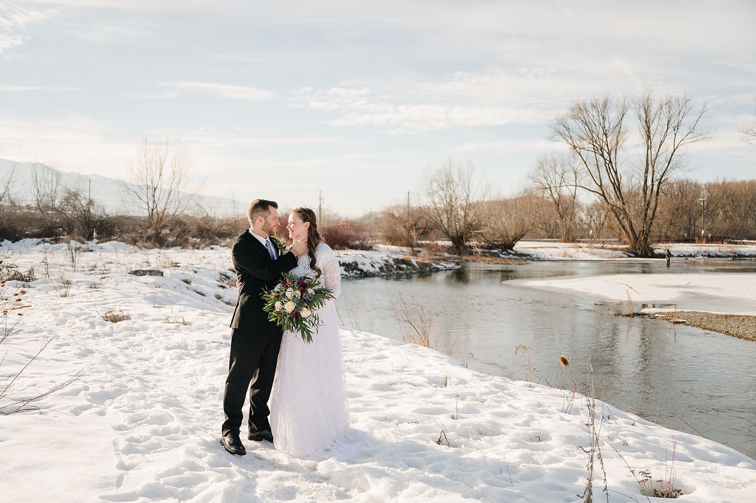 A romantic winter wedding photo by a snowy riverbank.